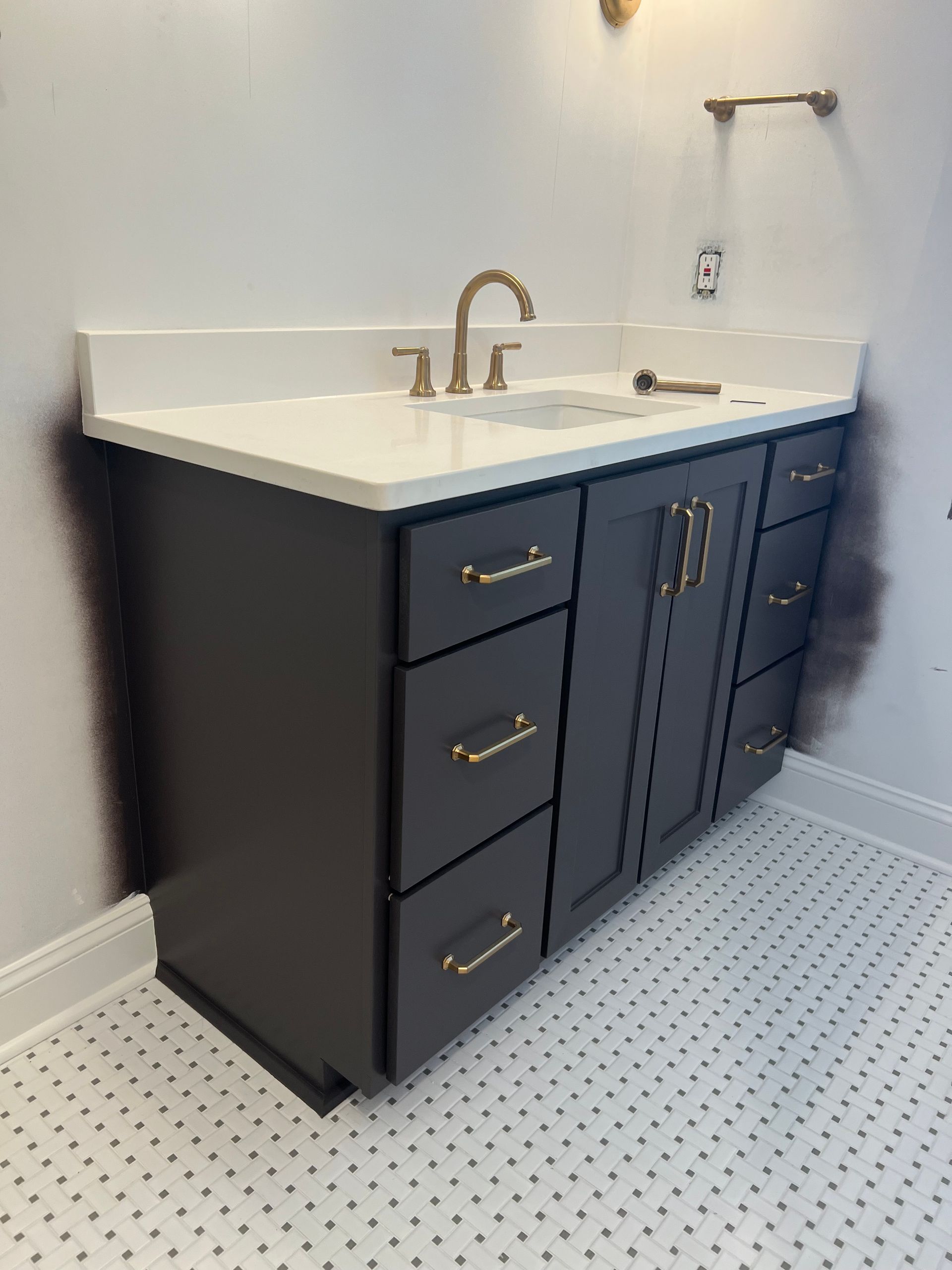 Dark navy bathroom vanity with white countertop, brass faucet, and built-in sink in a tiled room