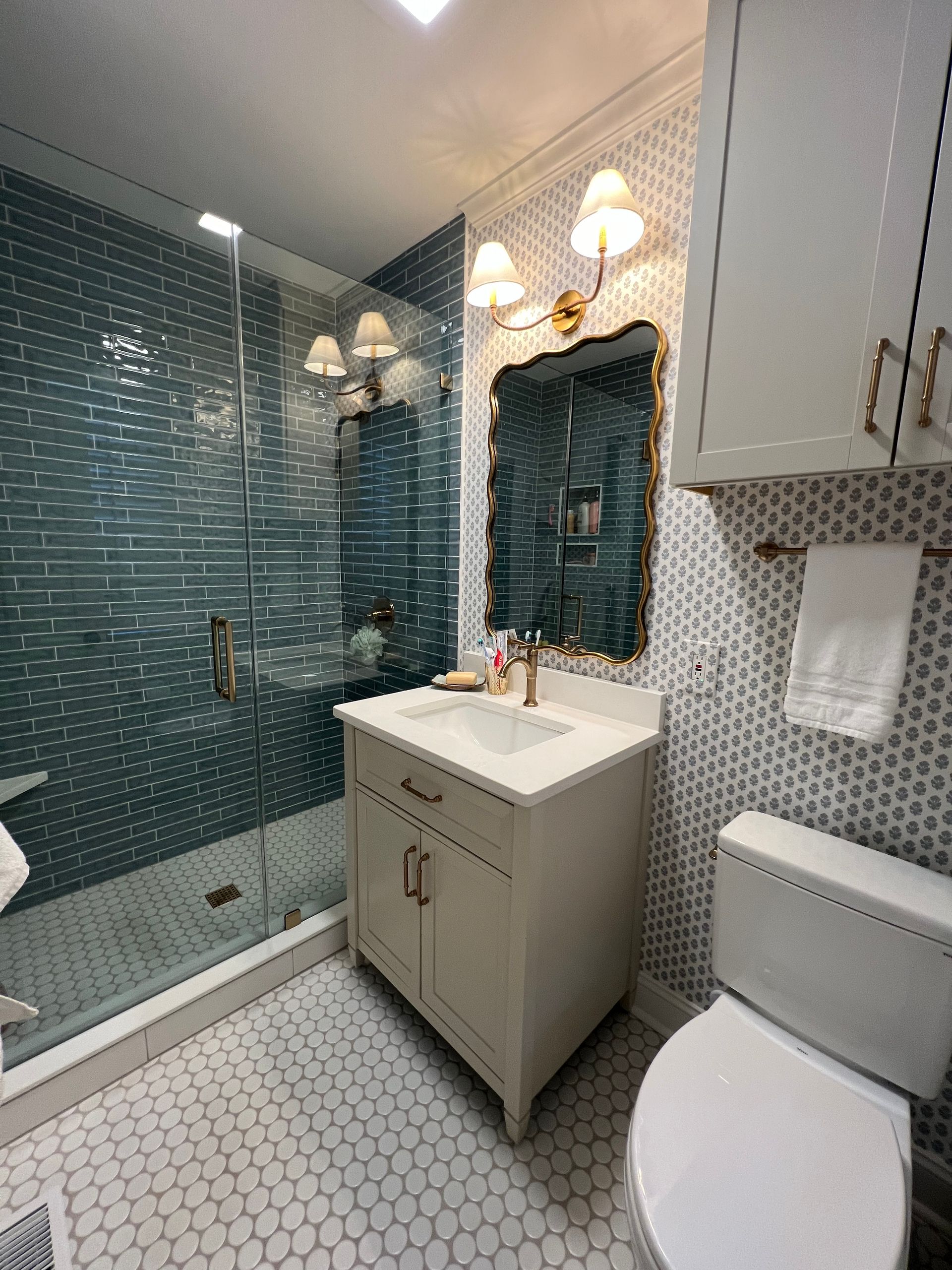 Small bathroom with blue tile shower, white vanity, ornate mirror, and toilet.