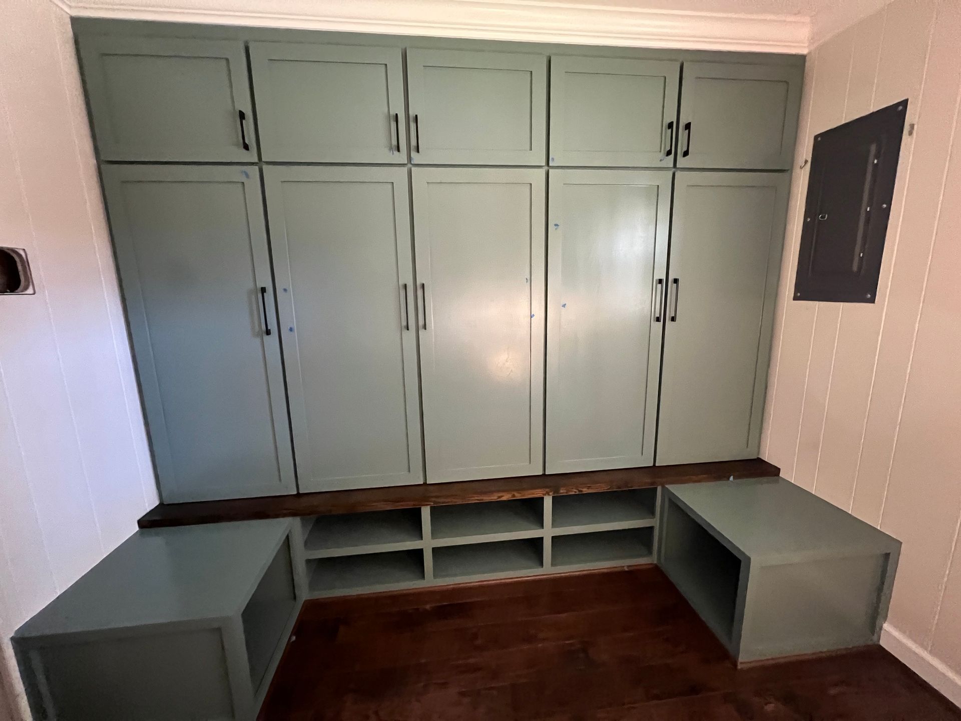 Built-in gray storage cabinets and benches in a small room with wood flooring