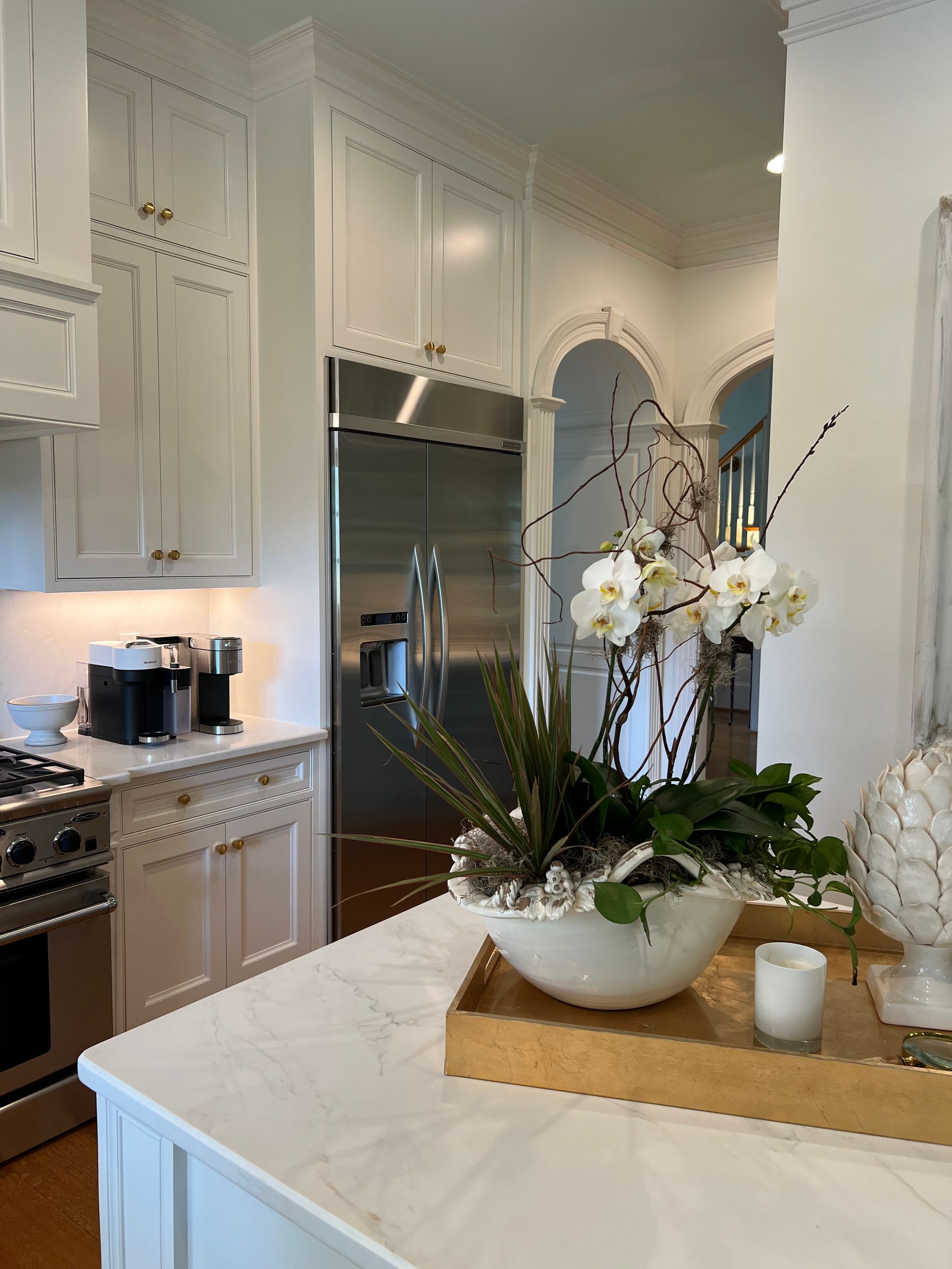 Bright white kitchen with island, marble counter, and floral centerpiece near stainless steel appliances.