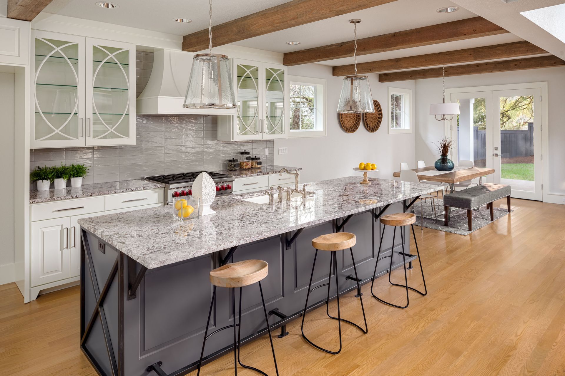Bright modern kitchen with granite island, stools, white cabinets, and hardwood floors
