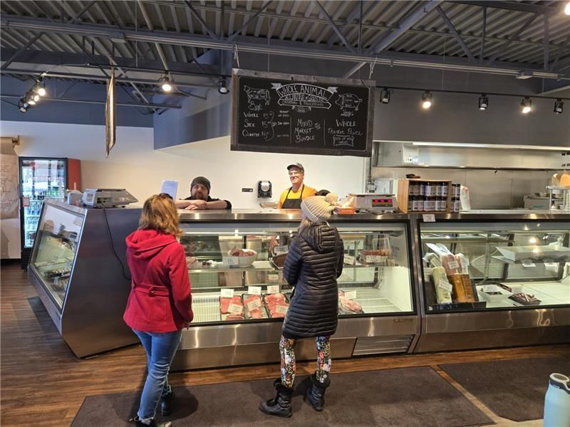 A woman in a red jacket is standing in front of a display case in a butcher shop.