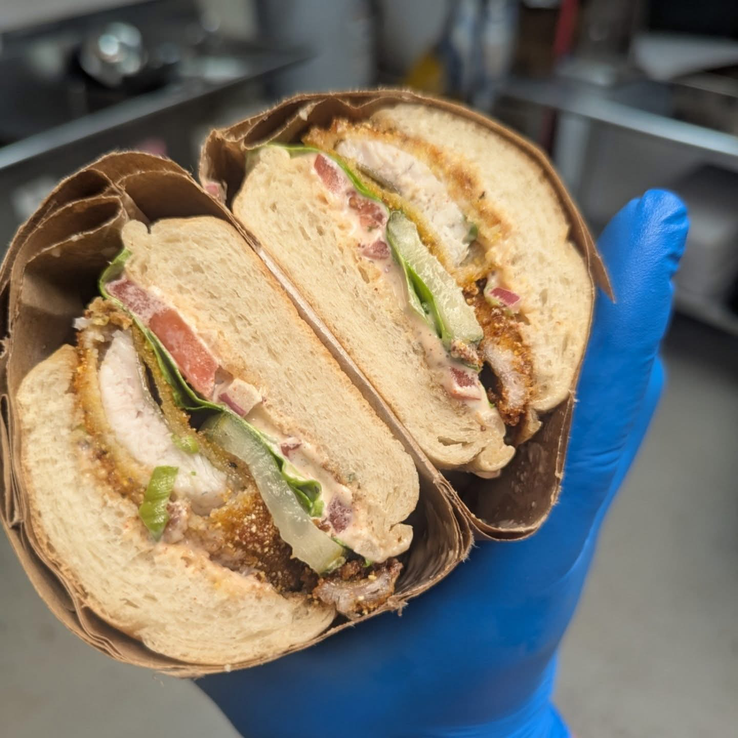 A person in a blue glove is holding a sandwich cut in half