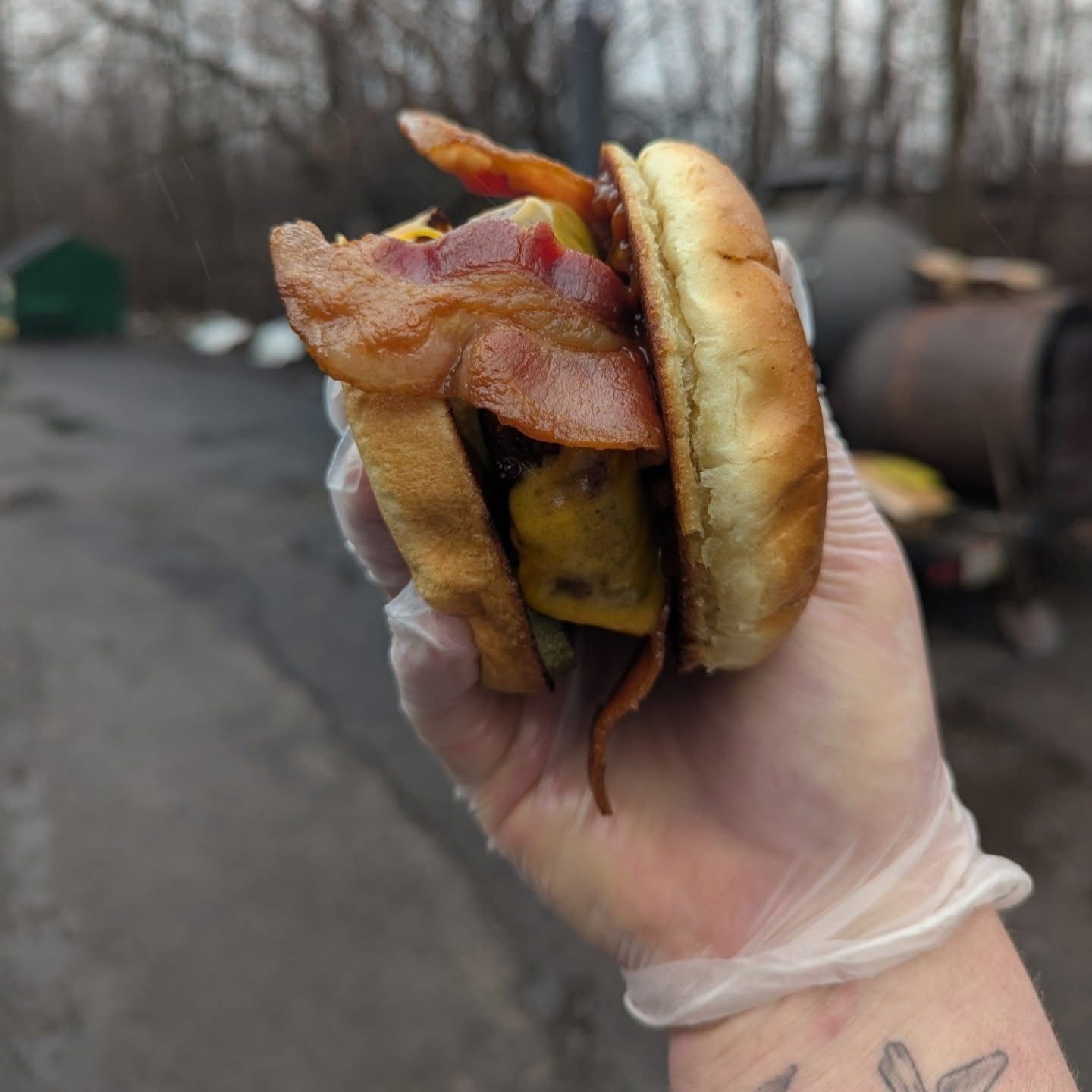 A person wearing gloves is holding a hamburger with bacon and cheese