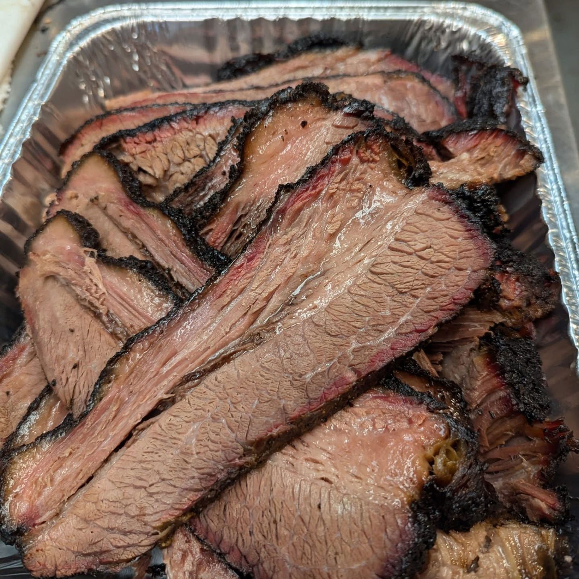 Aluminum foil container filled with sliced beef on a table.
