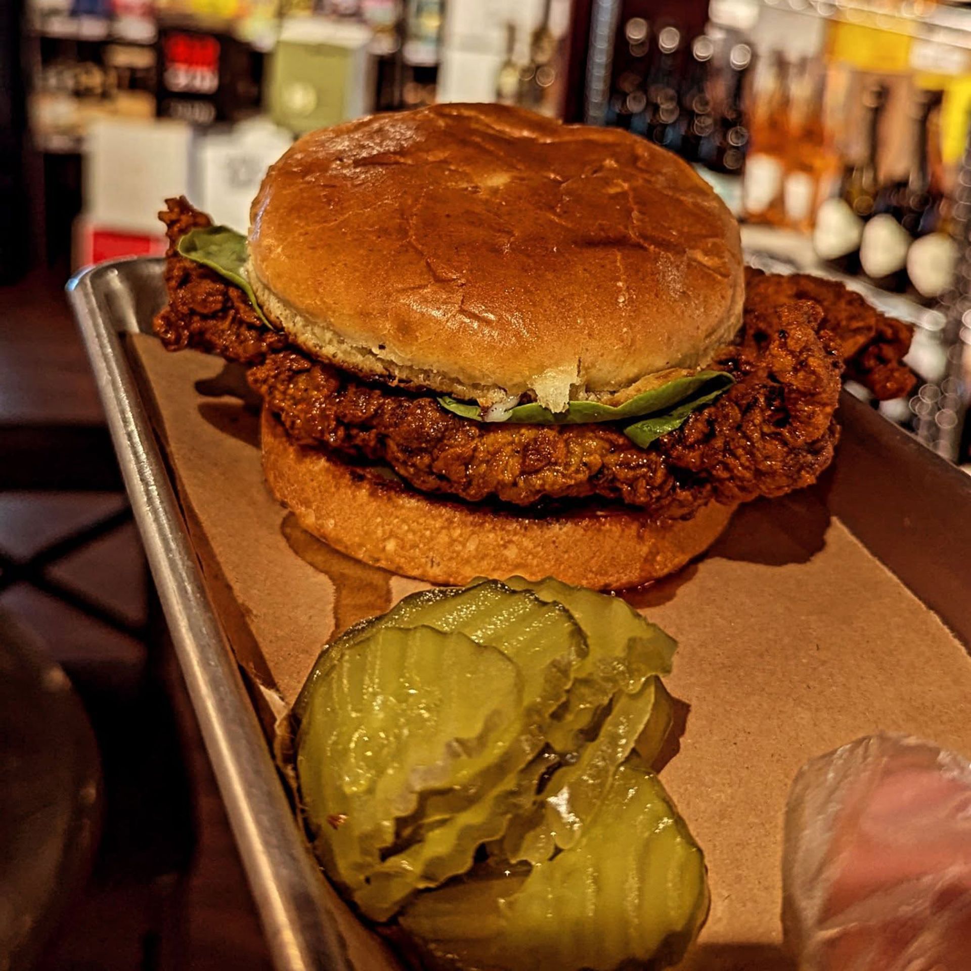 A person is holding a tray of food with a chicken sandwich and pickles on it.