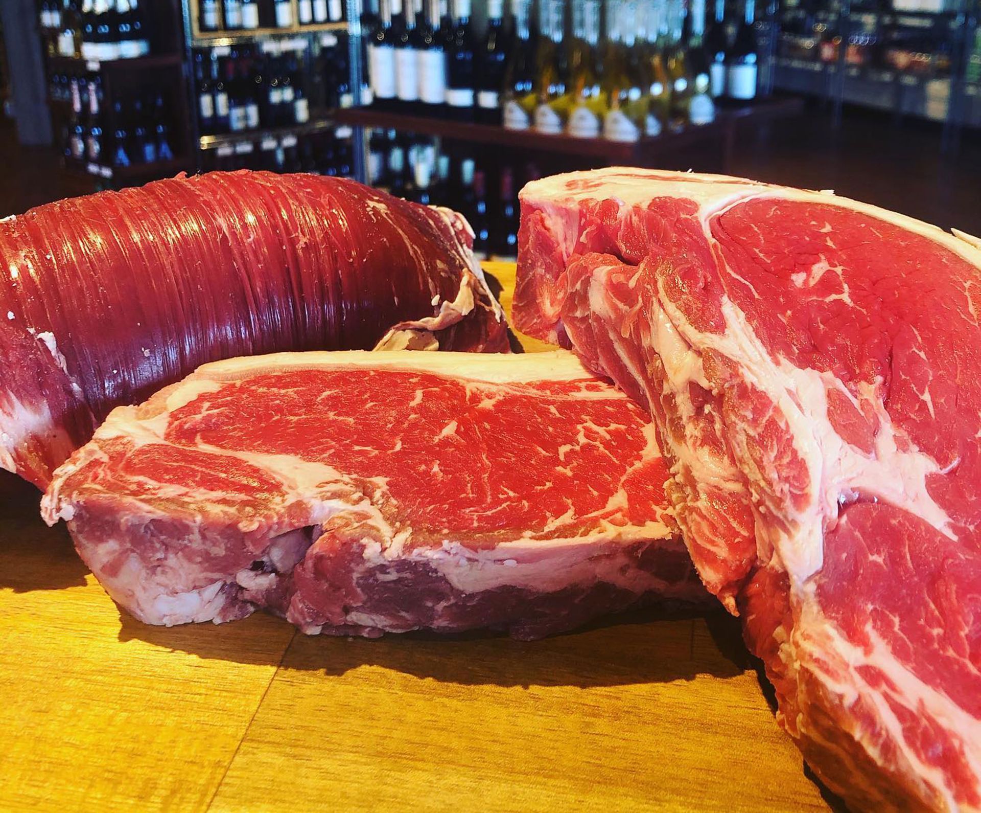 Two steaks and a sausage on a wooden cutting board