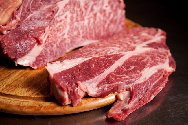 Raw, marbled beef steaks on a wooden cutting board, ready for cooking.