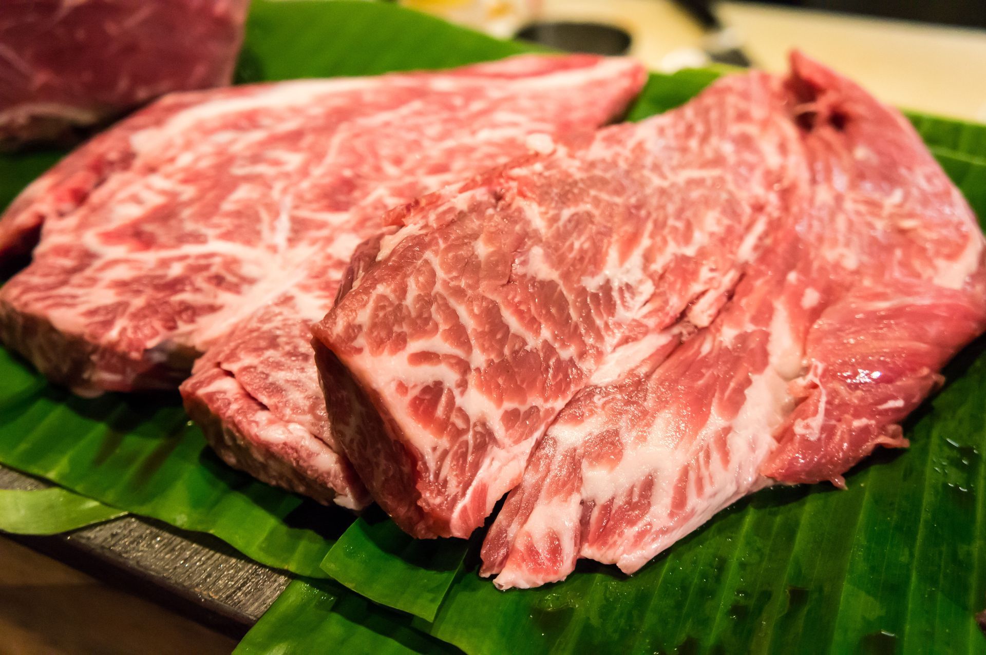 Raw, marbled beef steaks on green banana leaves.