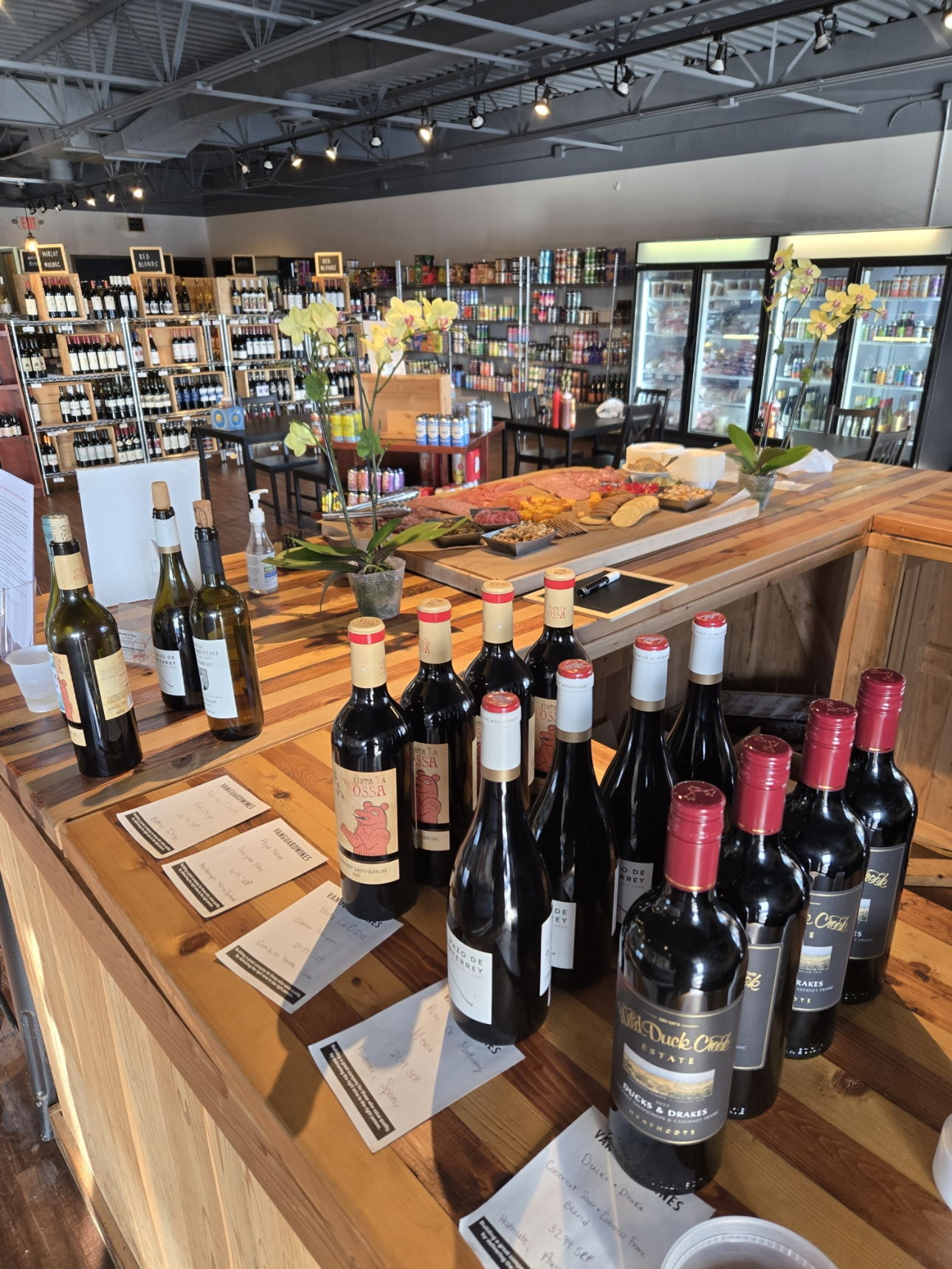 A bunch of wine bottles are sitting on a wooden table in a store.