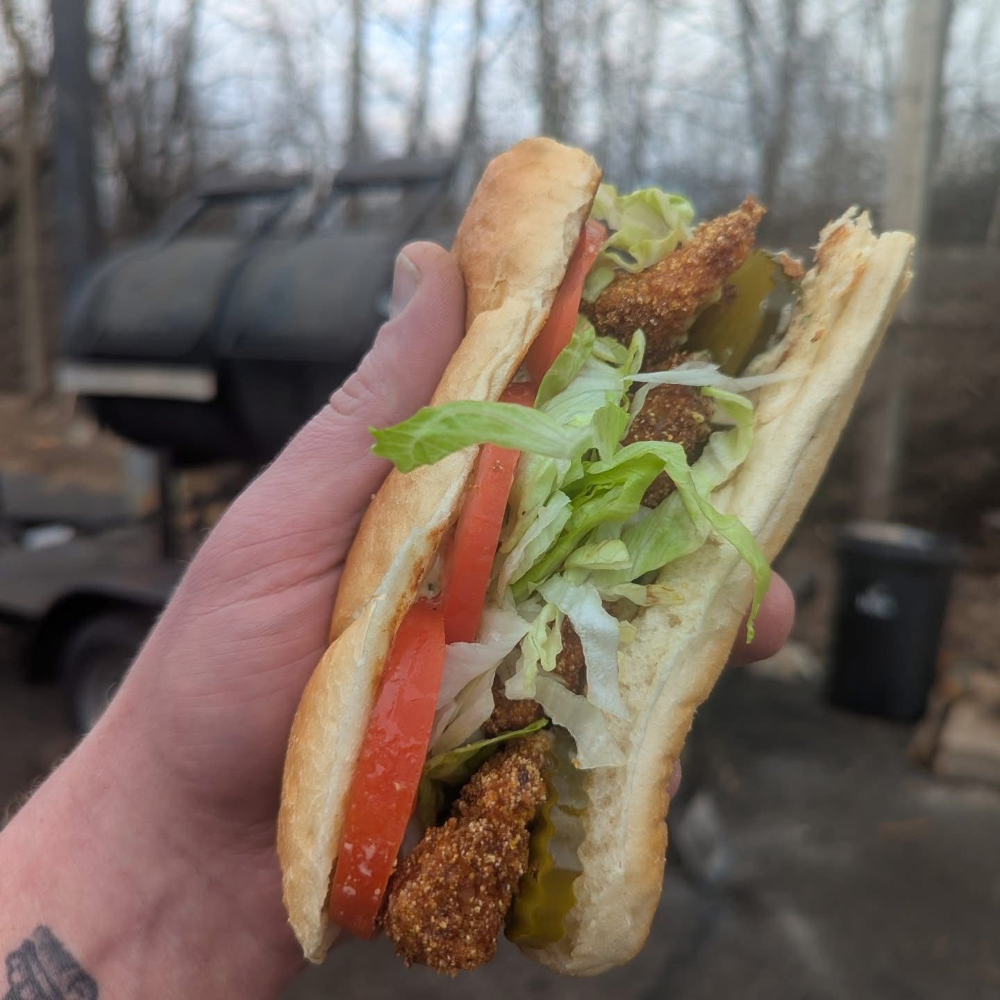 A person is holding a fried chicken sub sandwich with lettuce , tomato and pickles.