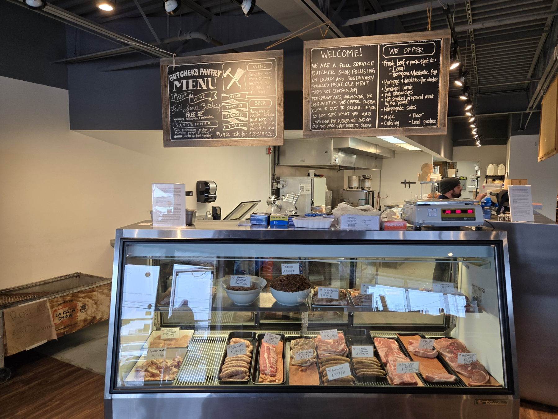 A butcher shop with a display case filled with meat and a menu hanging from the ceiling.