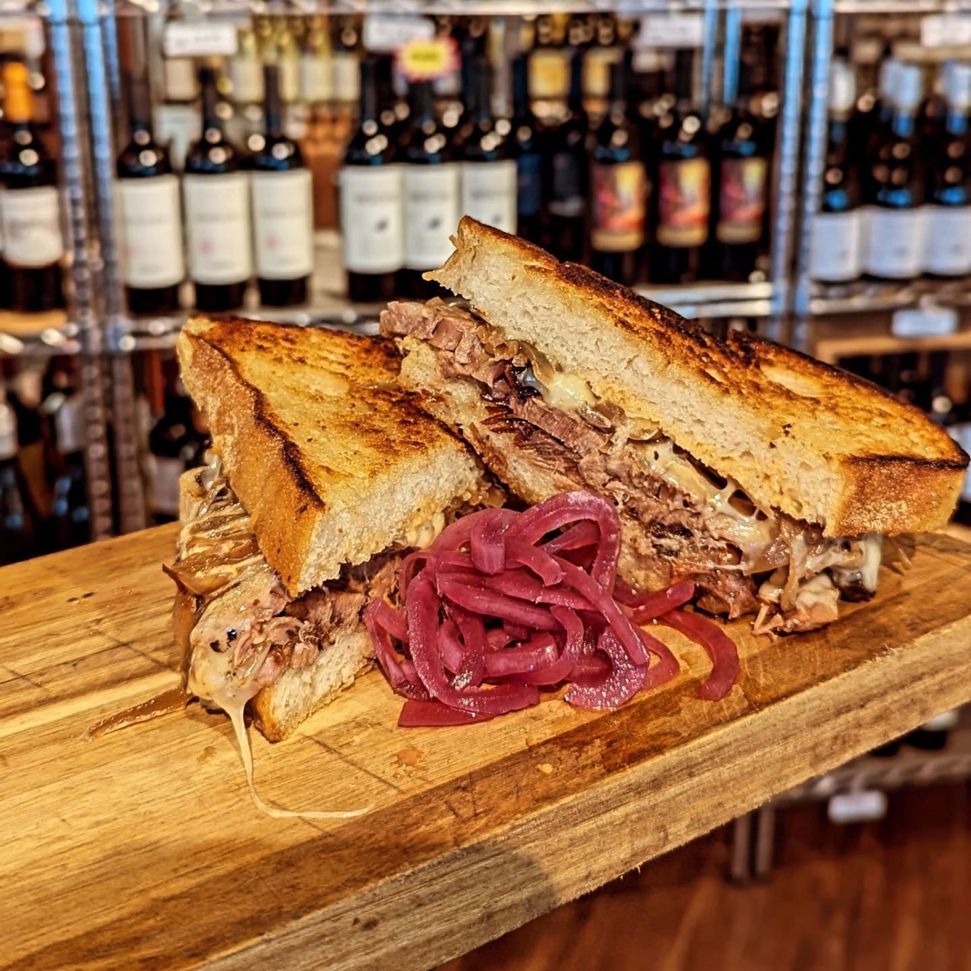 A sandwich with meat and onions on a wooden cutting board.