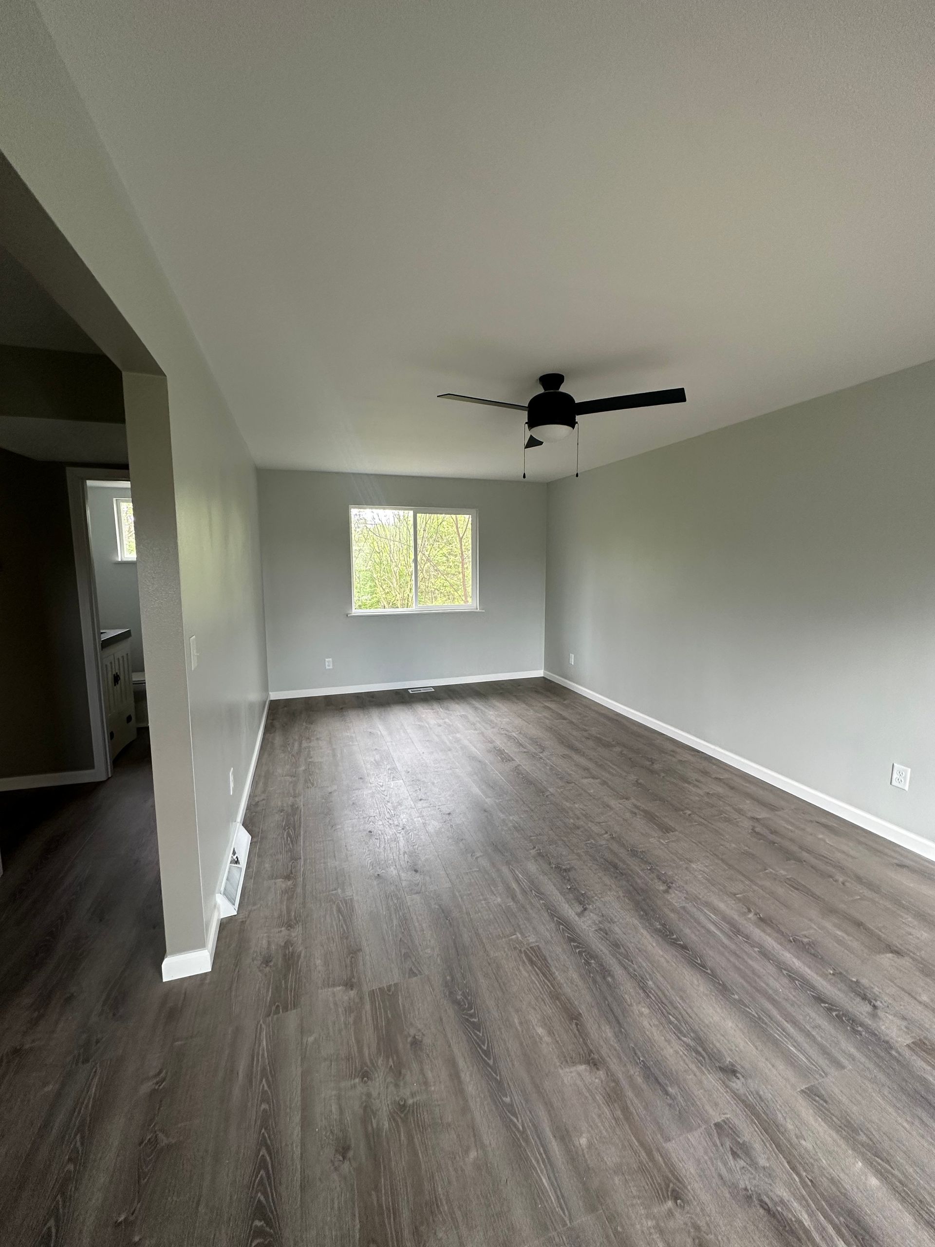 An empty living room with hardwood floors and a ceiling fan.