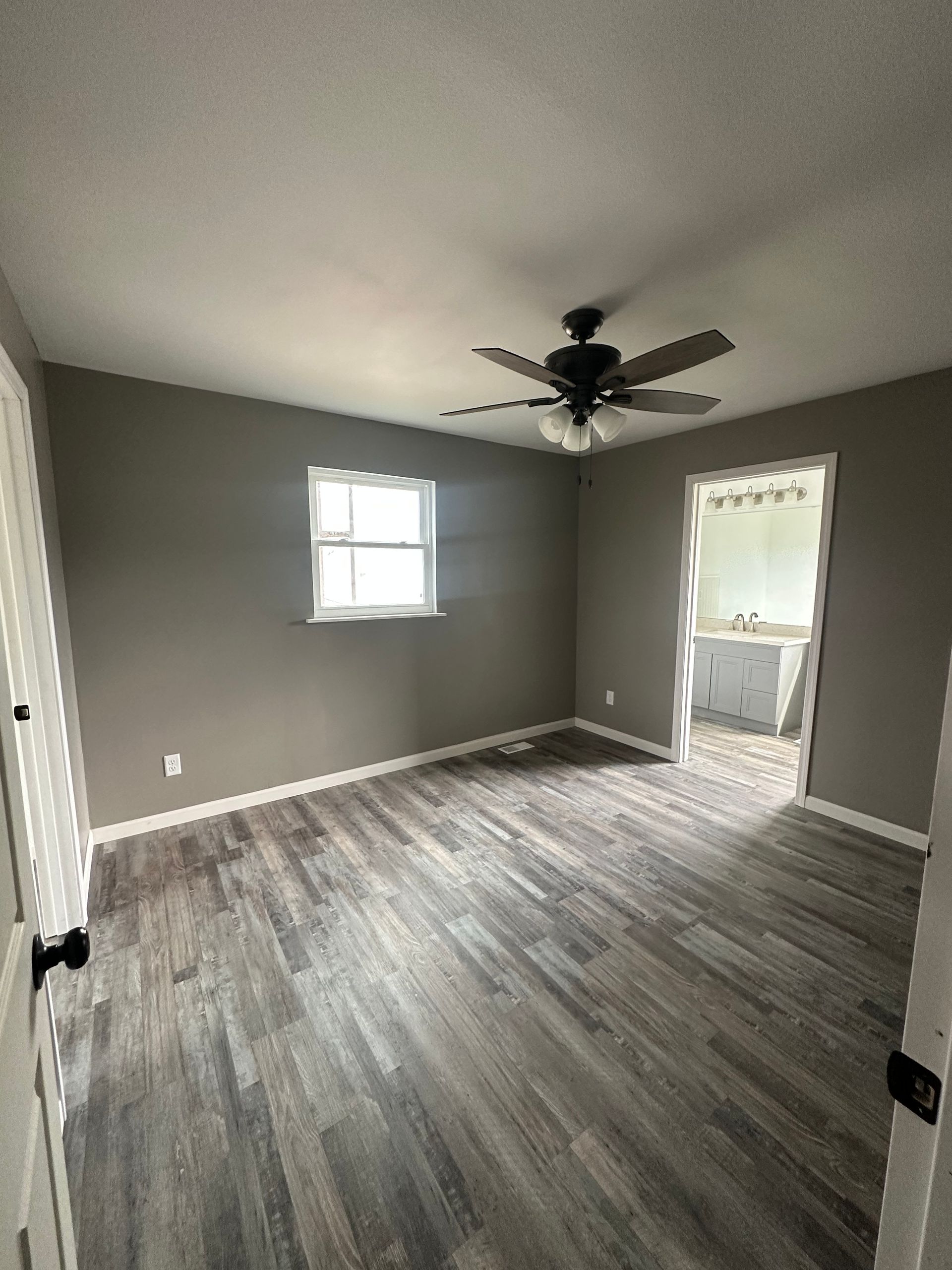 An empty room with a ceiling fan and a window.