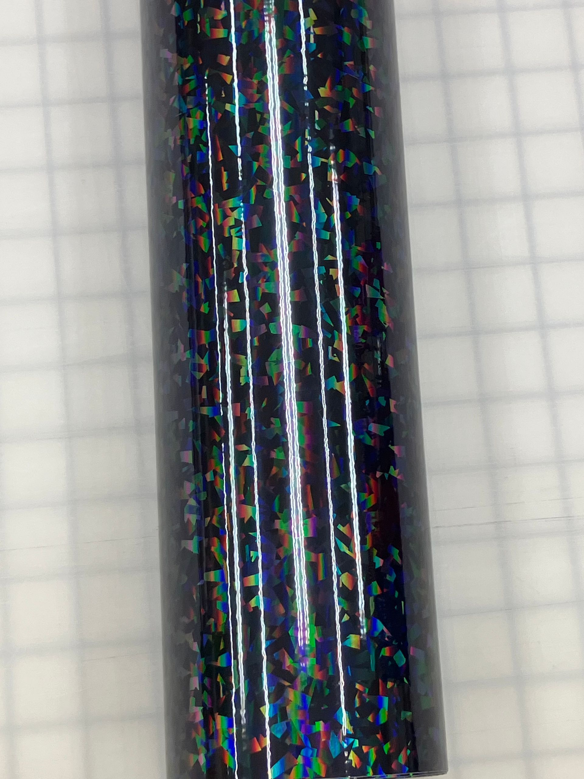 Close-up of a glossy black cylindrical rod with colorful speckles against graph paper.