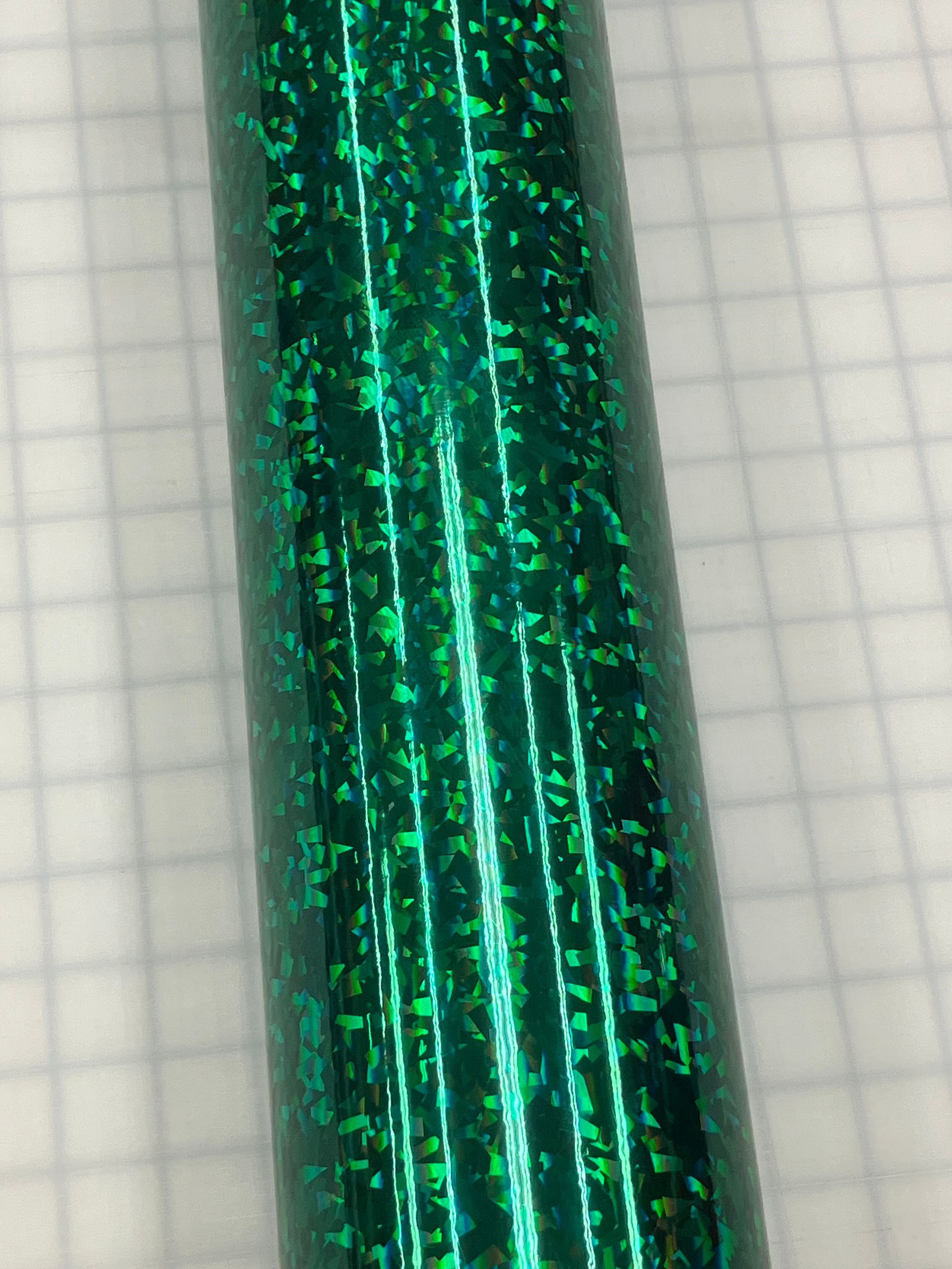 Close-up of a shiny green glittery cylindrical object against a light grid background