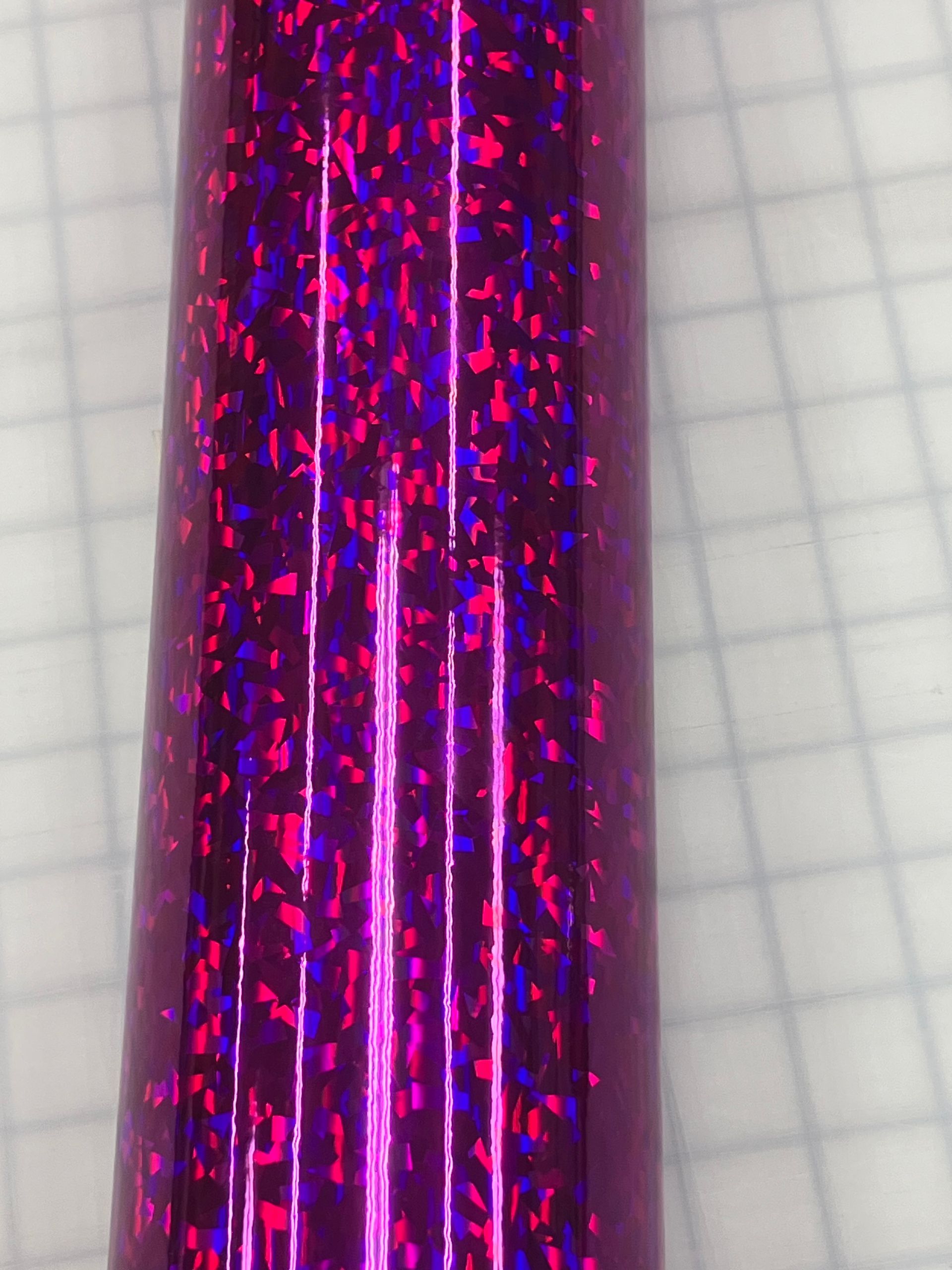 Close-up of a glittery purple and pink cylindrical object against a light grid background