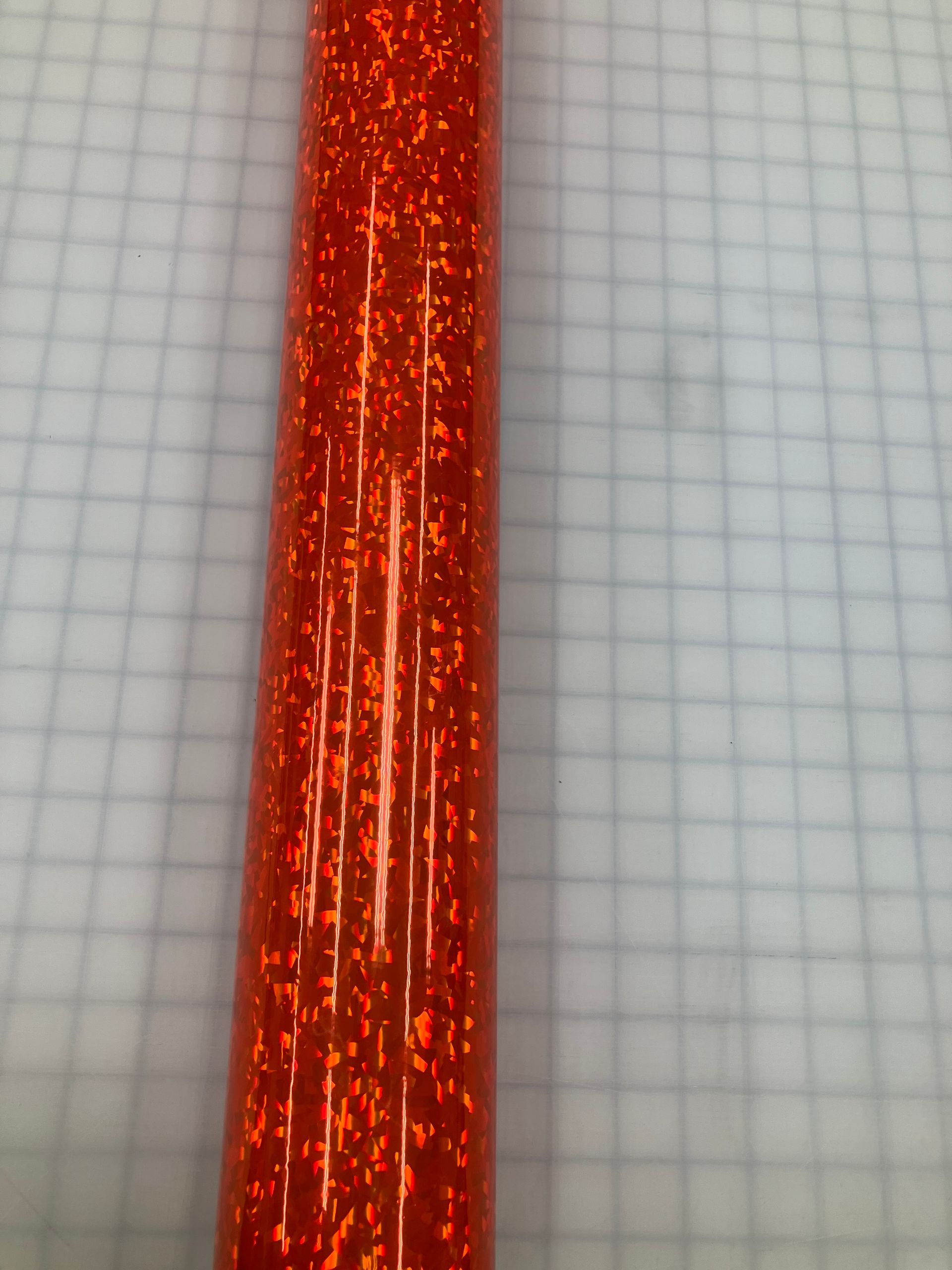 Close-up of a glittery red-orange textured strip on a light gray grid background