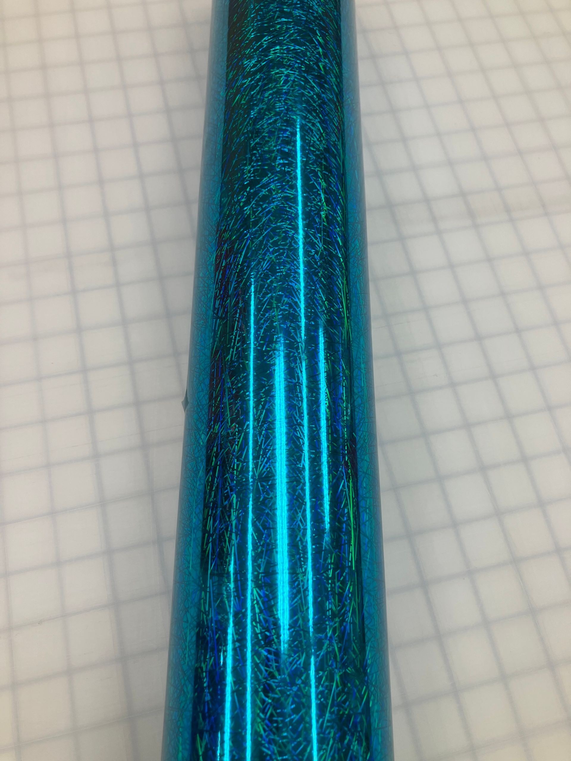 Close-up of a shiny metallic blue cylindrical object against graph paper background