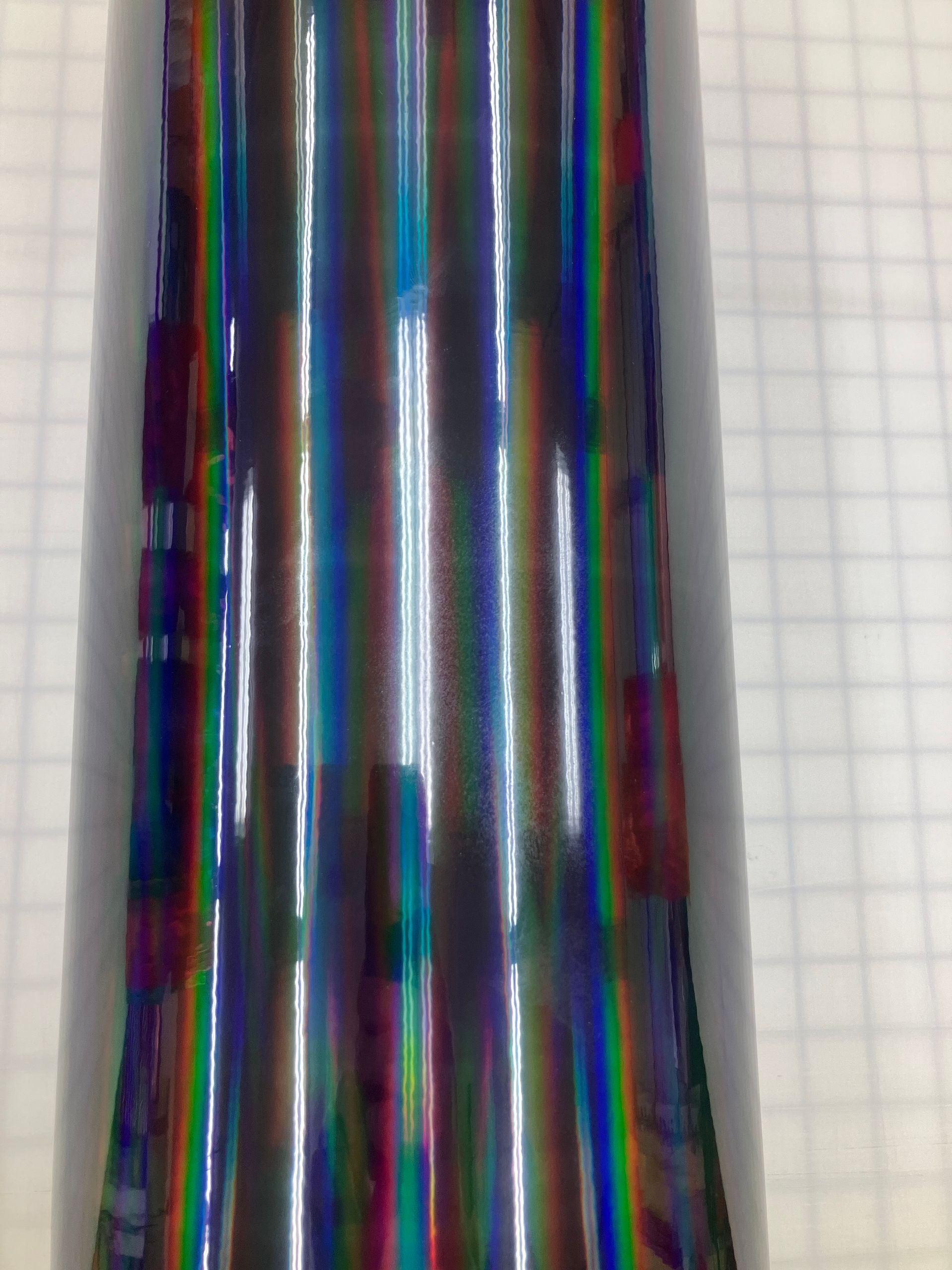 Close-up of a shiny metallic cylindrical object with rainbow reflections on a light background