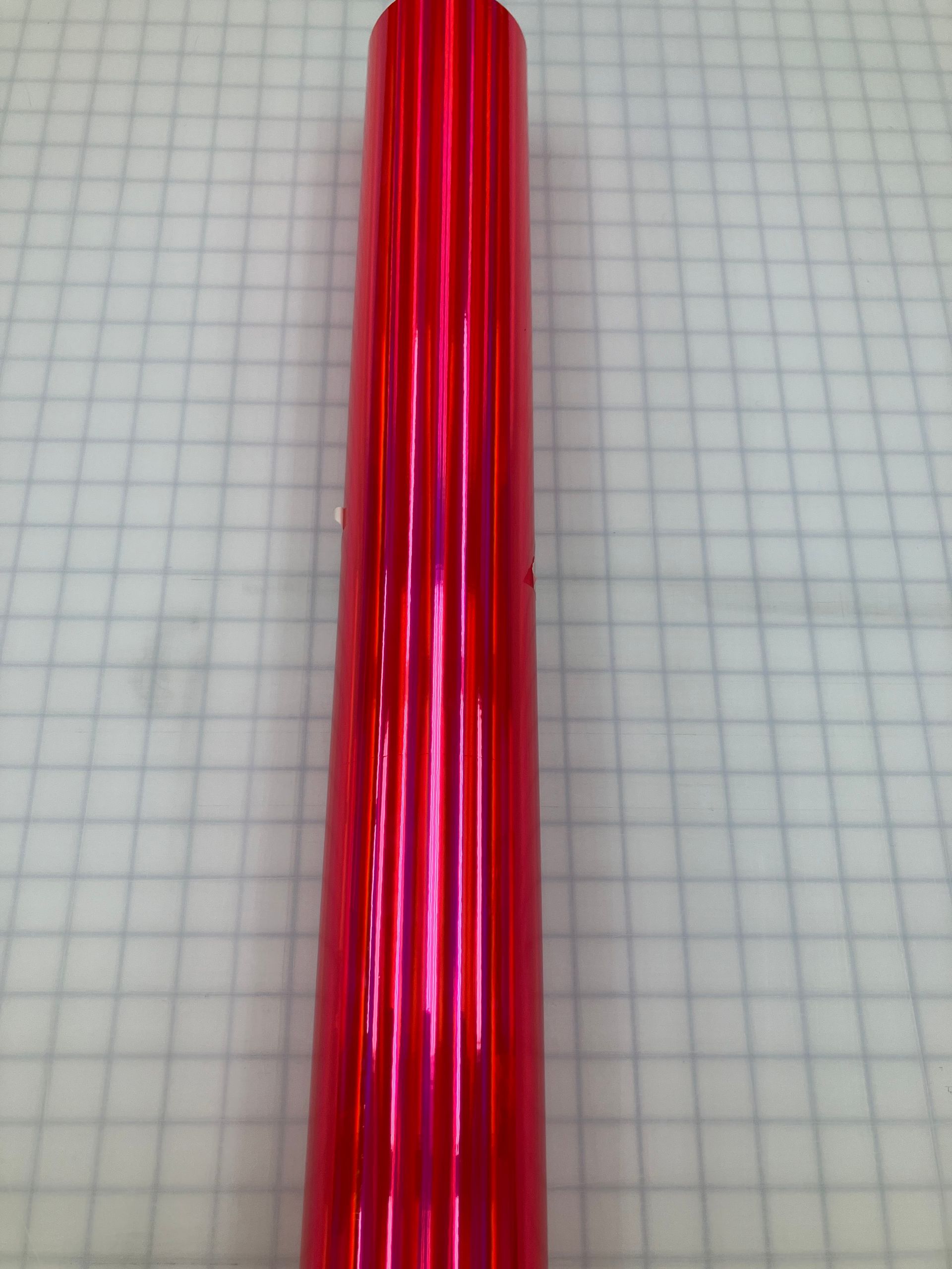 Red translucent ribbed plastic tube standing upright on graph paper.