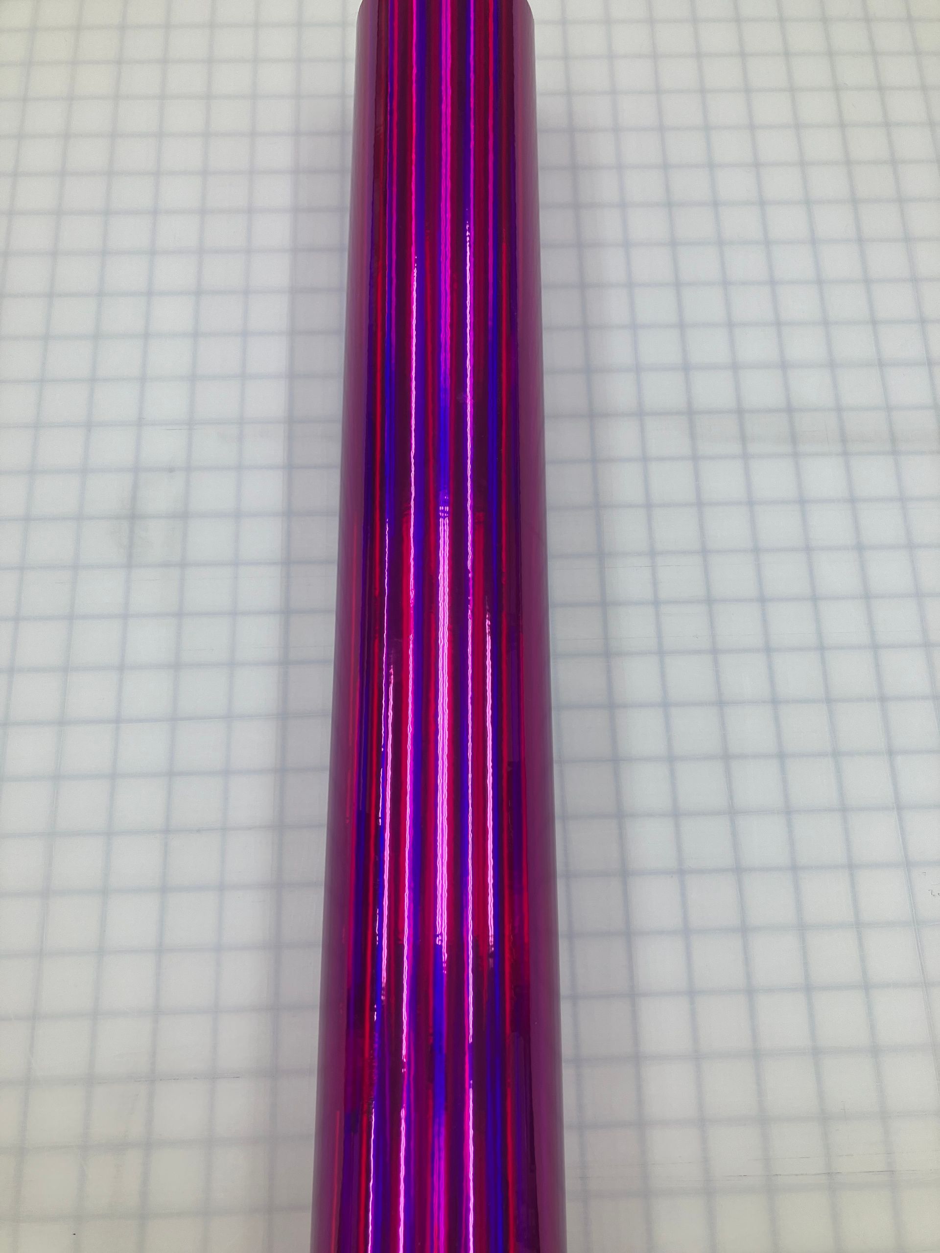 Shiny metallic magenta cylindrical object standing on graph paper