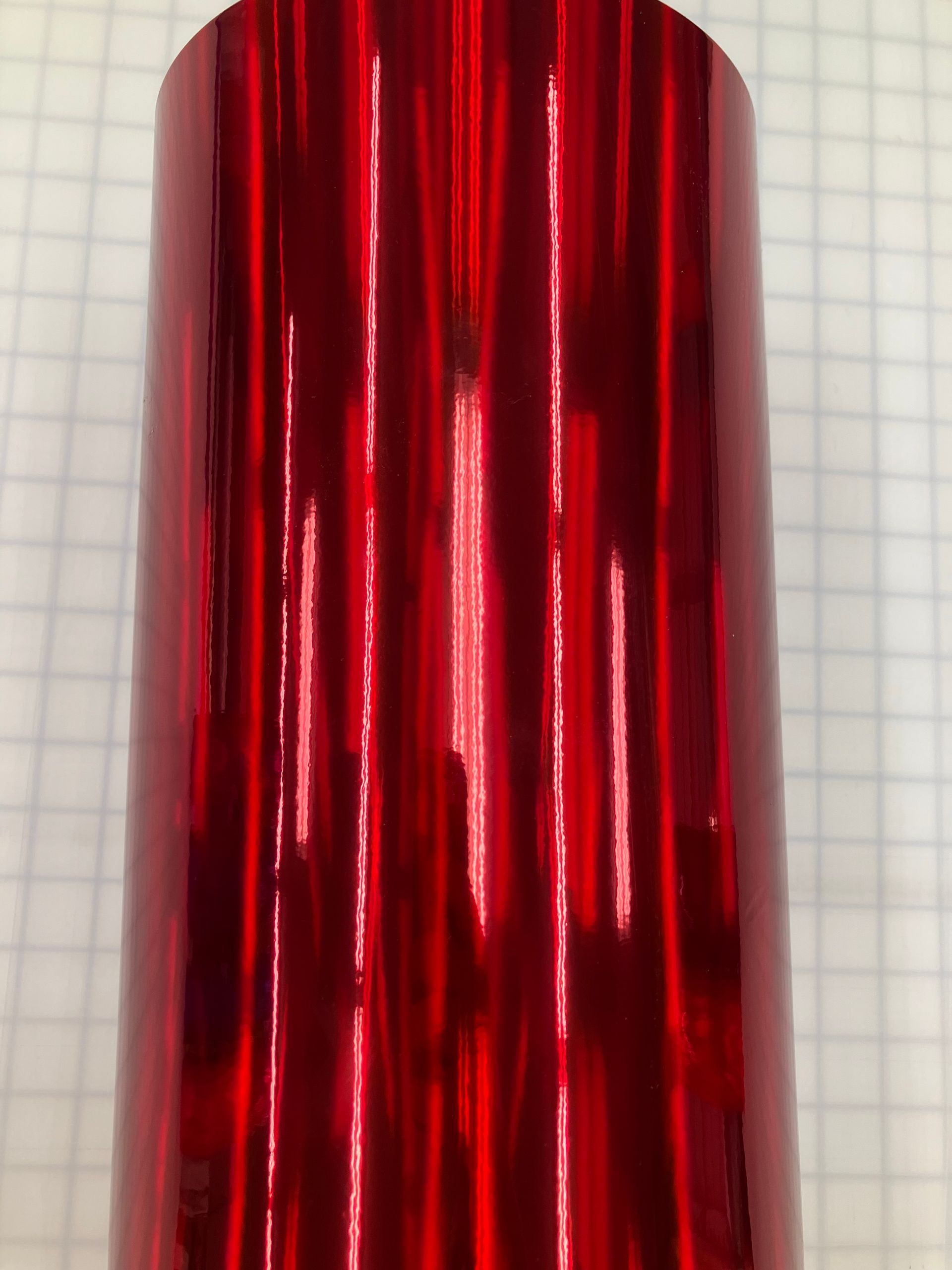 Shiny red metallic cylinder standing upright against graph paper
