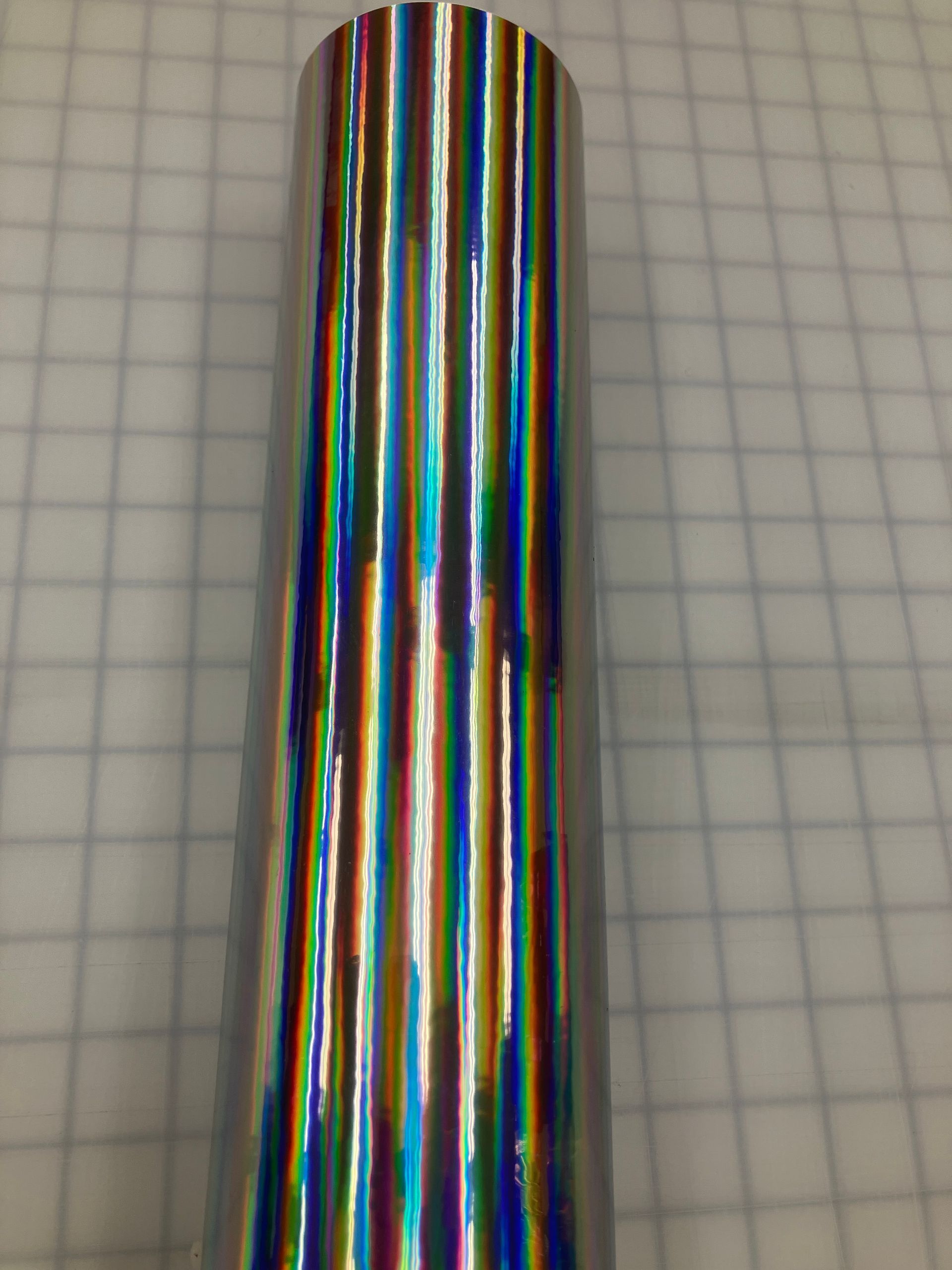 Vertical iridescent metallic cylinder with rainbow reflections on graph paper