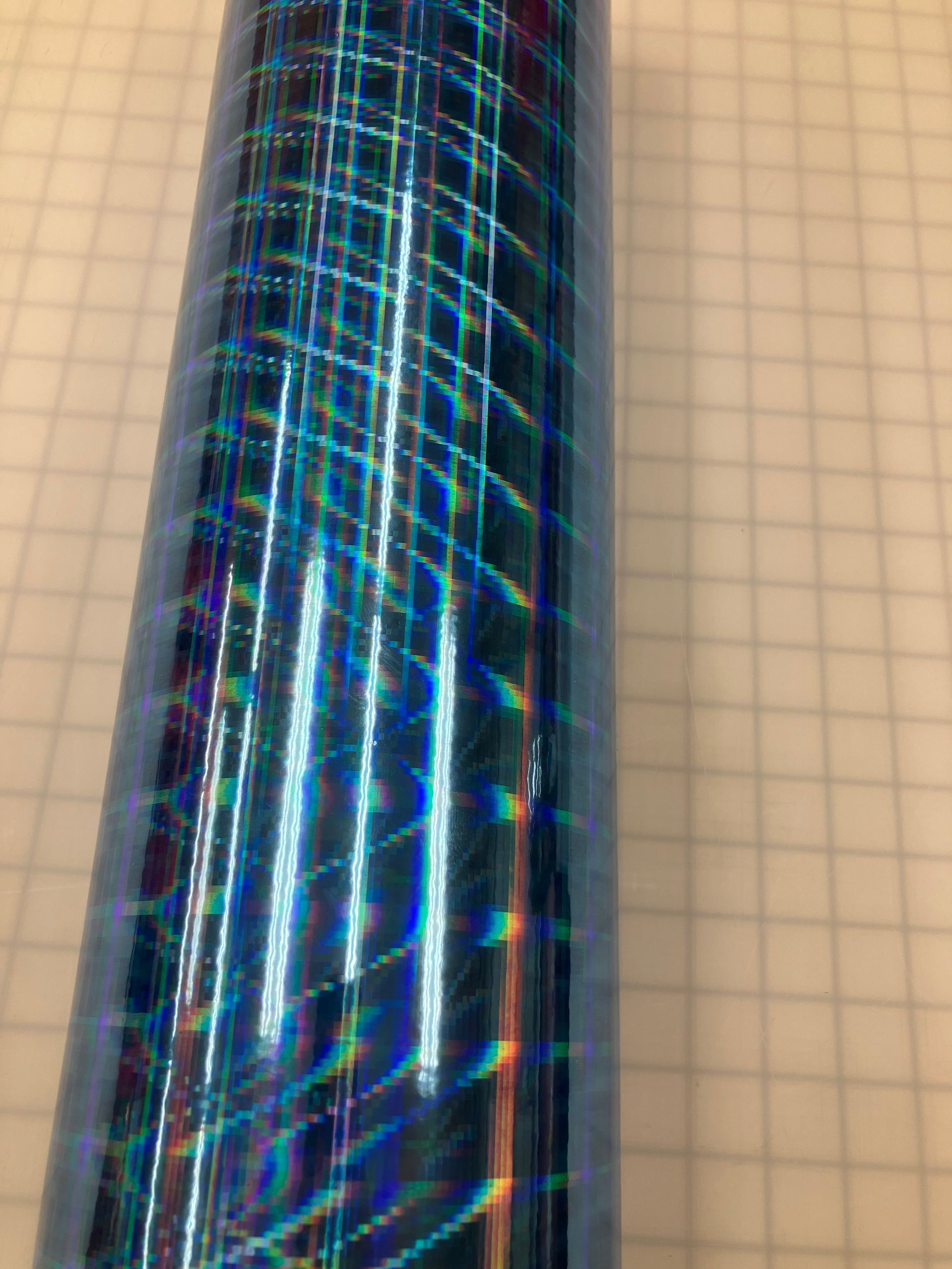 Close-up of a shiny iridescent blue cylindrical object against a beige grid background