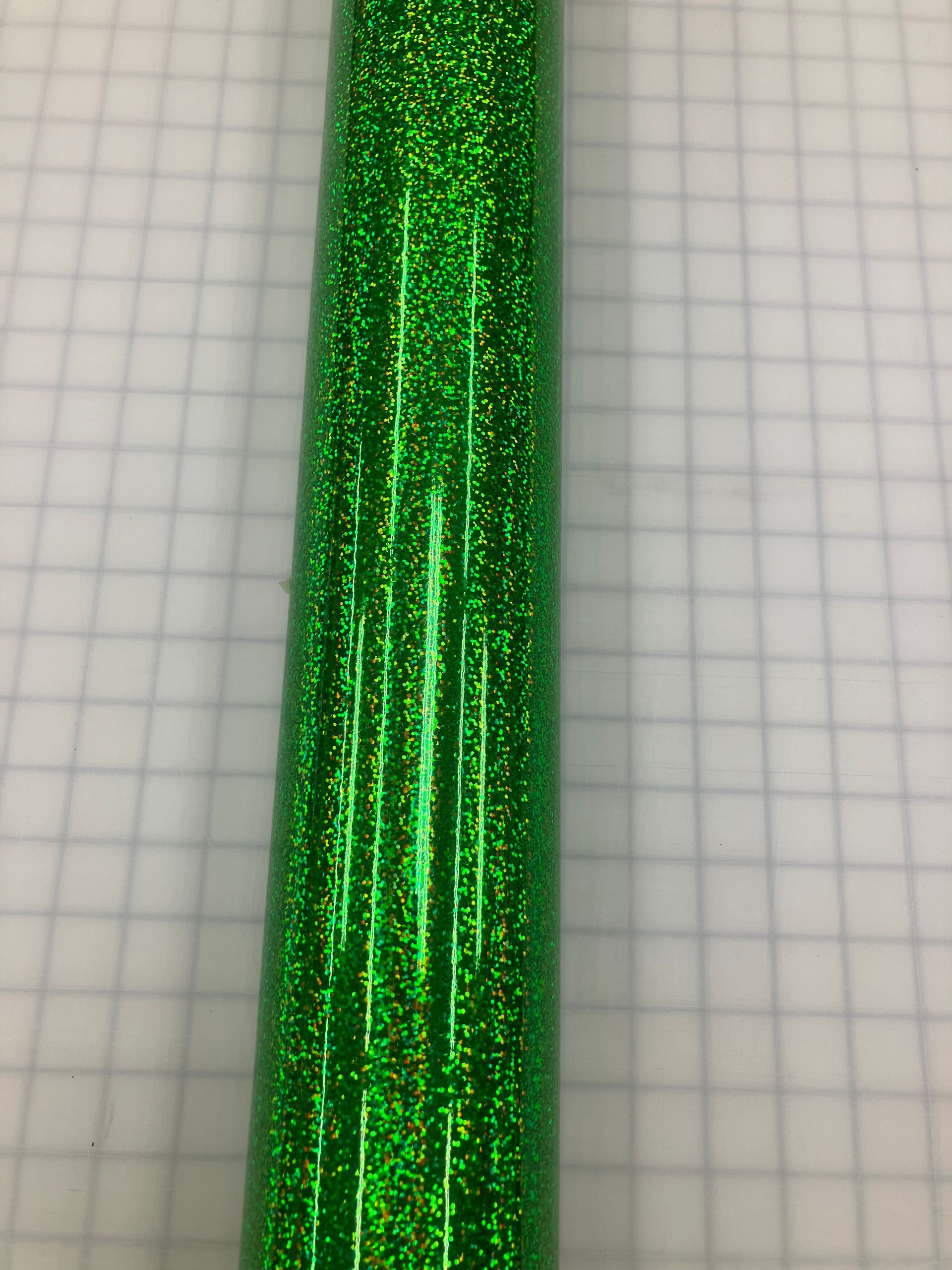 Close-up of a shiny green glittery cylindrical object on graph paper.
