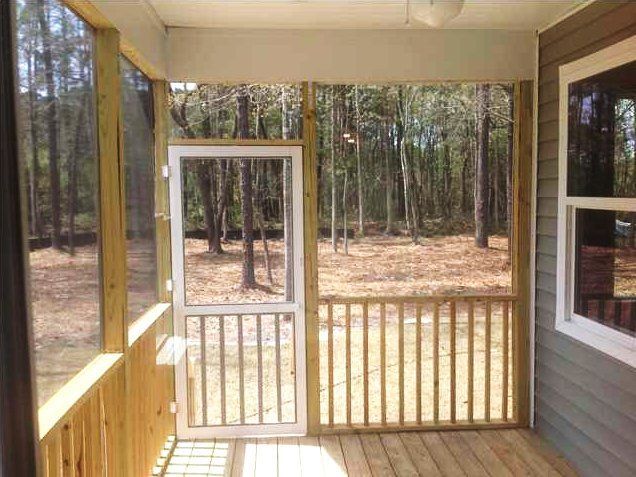 A screened in porch with a screen door and a view of the woods.