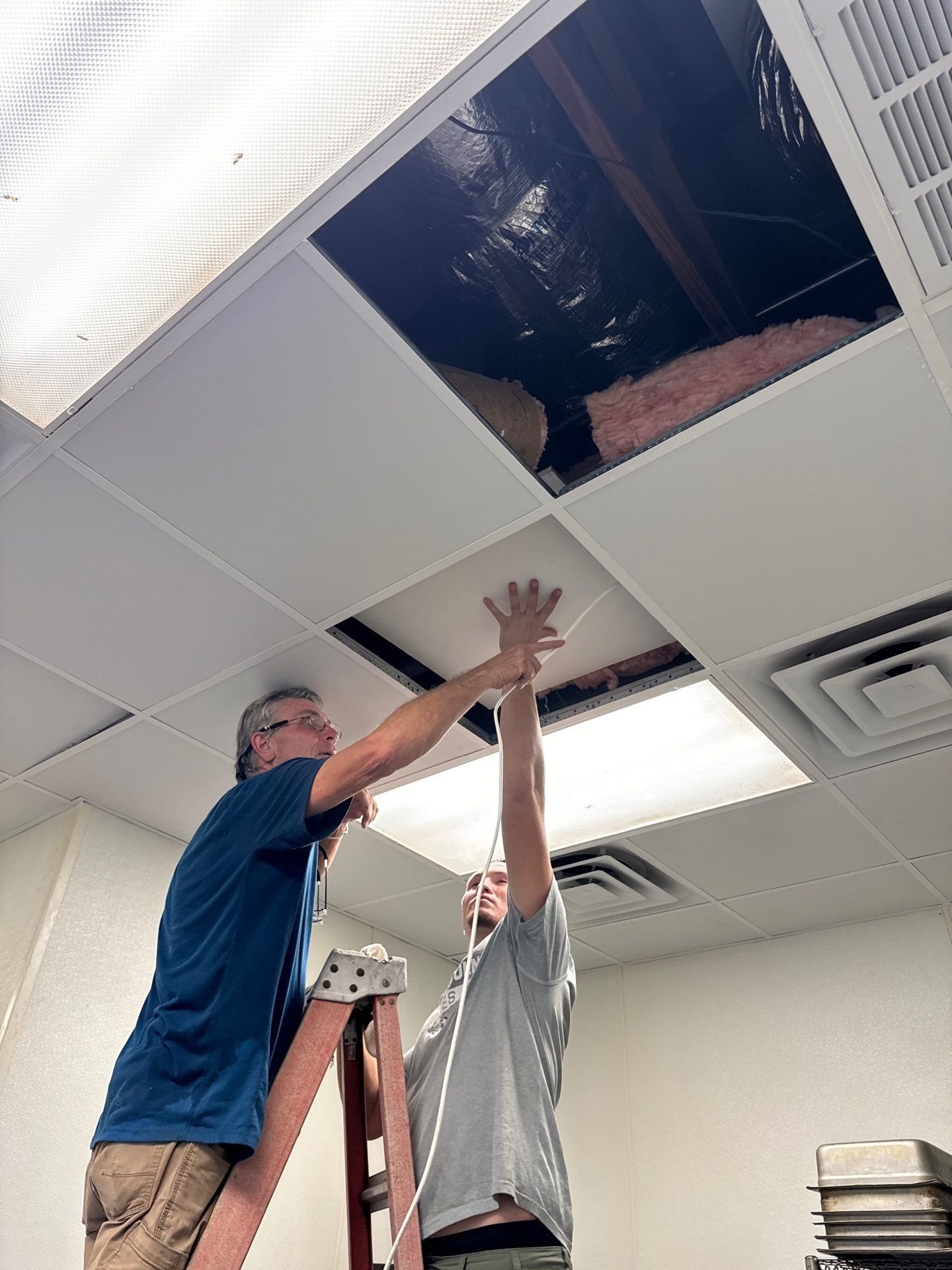 Two men are working on a ceiling in a room.