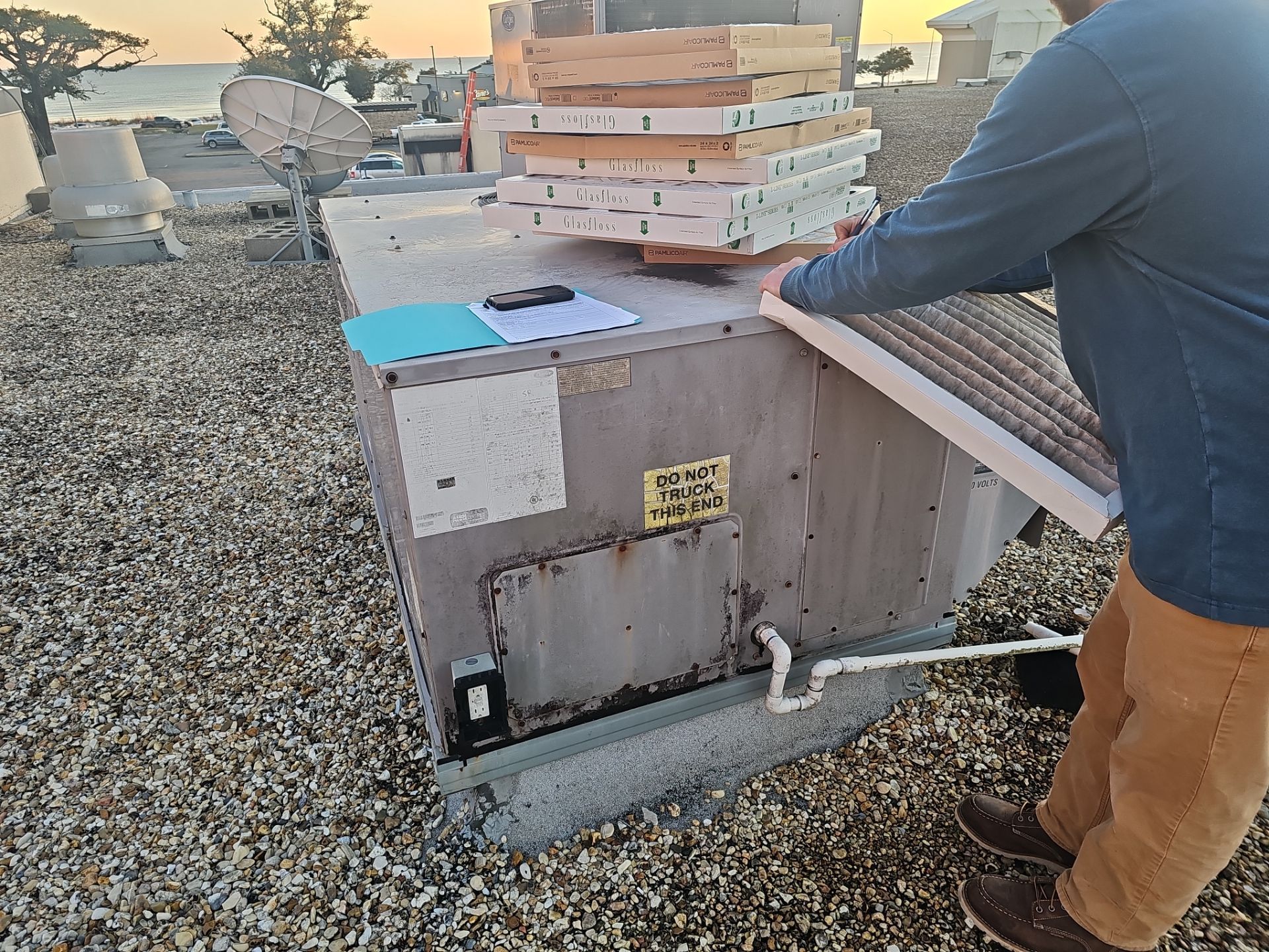 A man is working on an air conditioner on a roof.