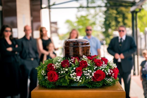 A group of people are standing around a urn with flowers at a funeral.