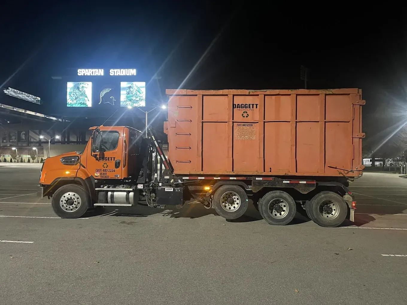 Orange dump truck parked at night under bright lights in an open lot
