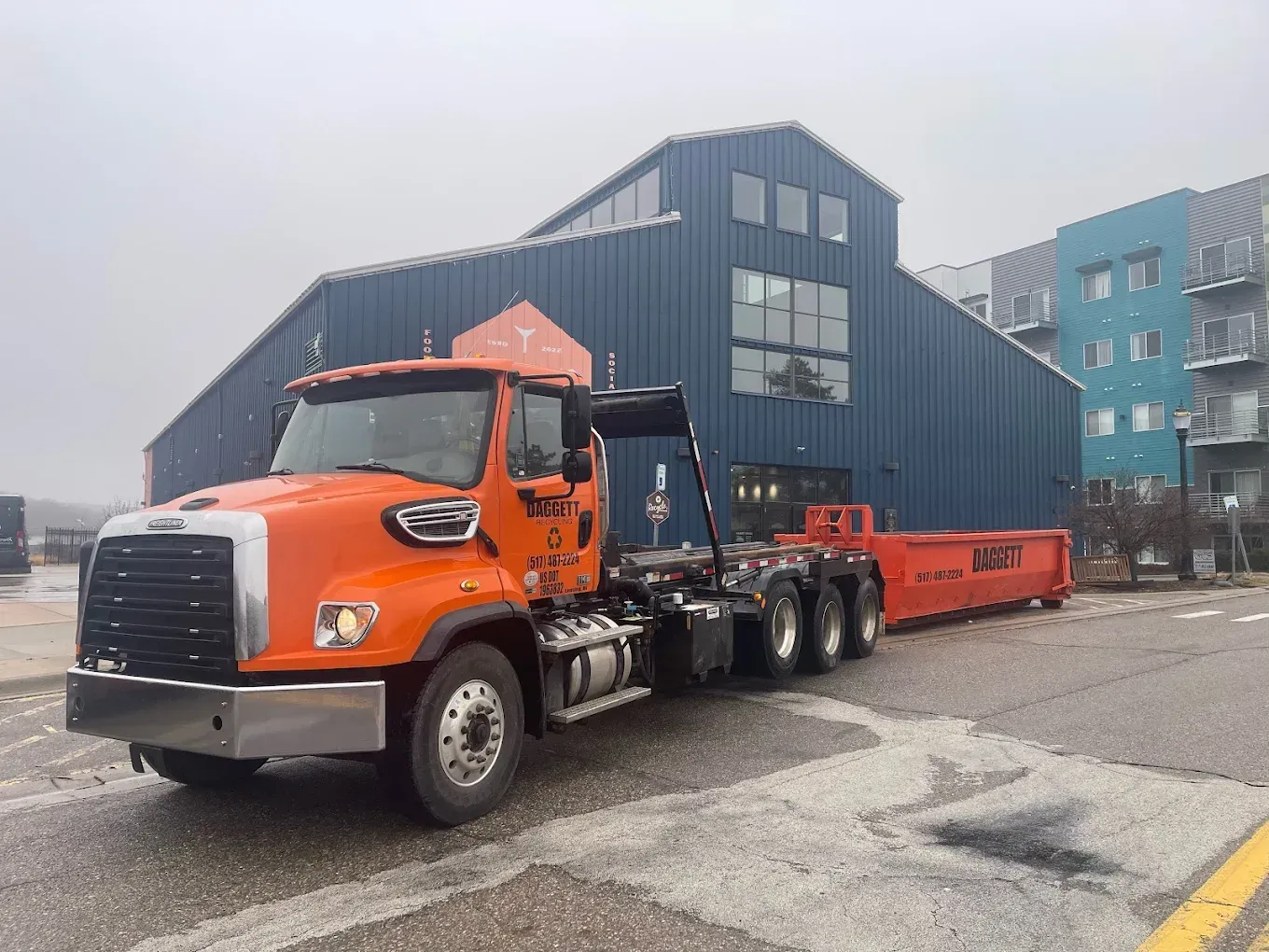 Orange semi-truck hauling a long red trailer in an industrial parking lot