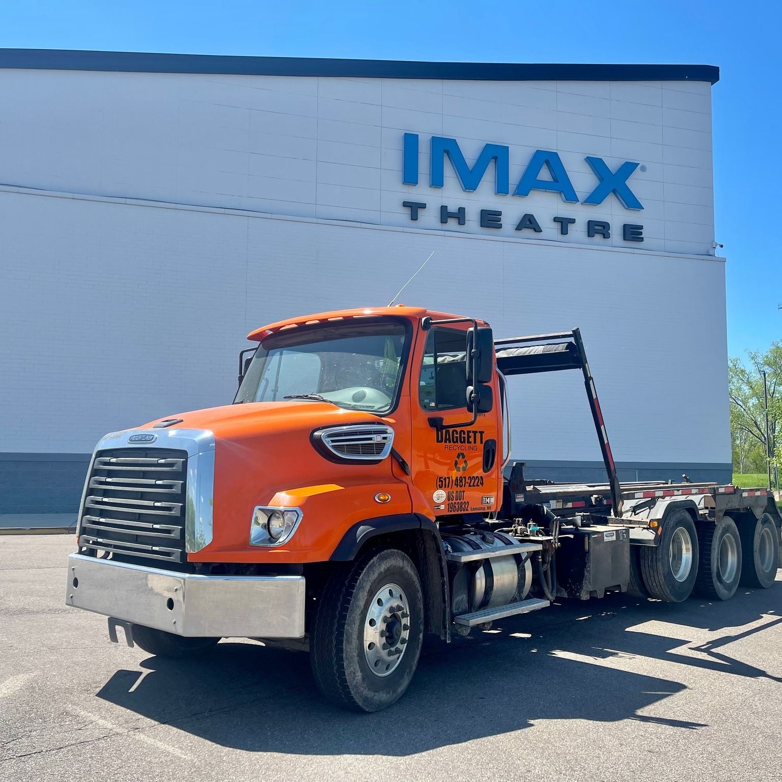 Orange tow truck parked outside an IMAX Theatre building on a sunny day