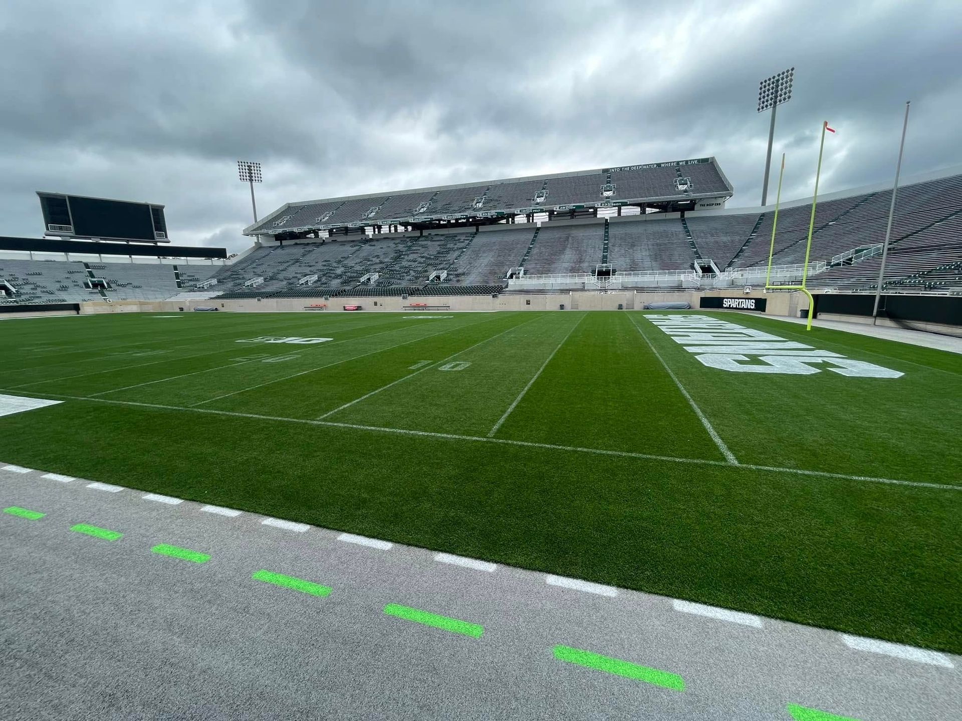 Empty football stadium with green field and gray seating under an overcast sky