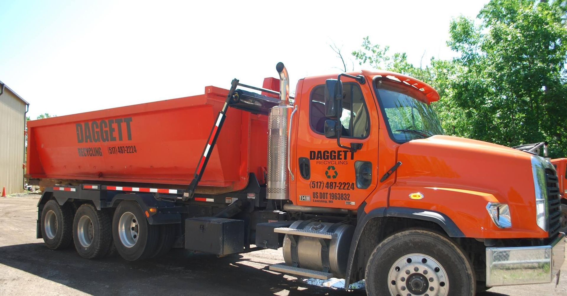 Orange dump truck parked outdoors on a sunny day, with black lettering on the side.