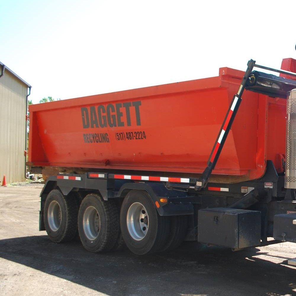 Red Daggett dump trailer parked outdoors beside a building in a gravel lot