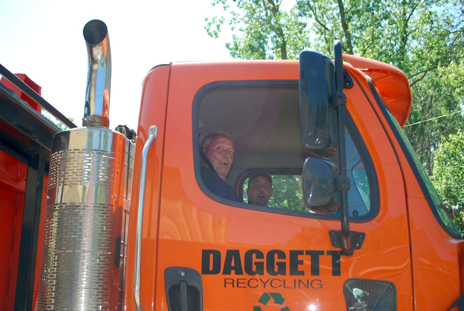 Orange Daggett Recycling truck cab with driver visible through the window outdoors