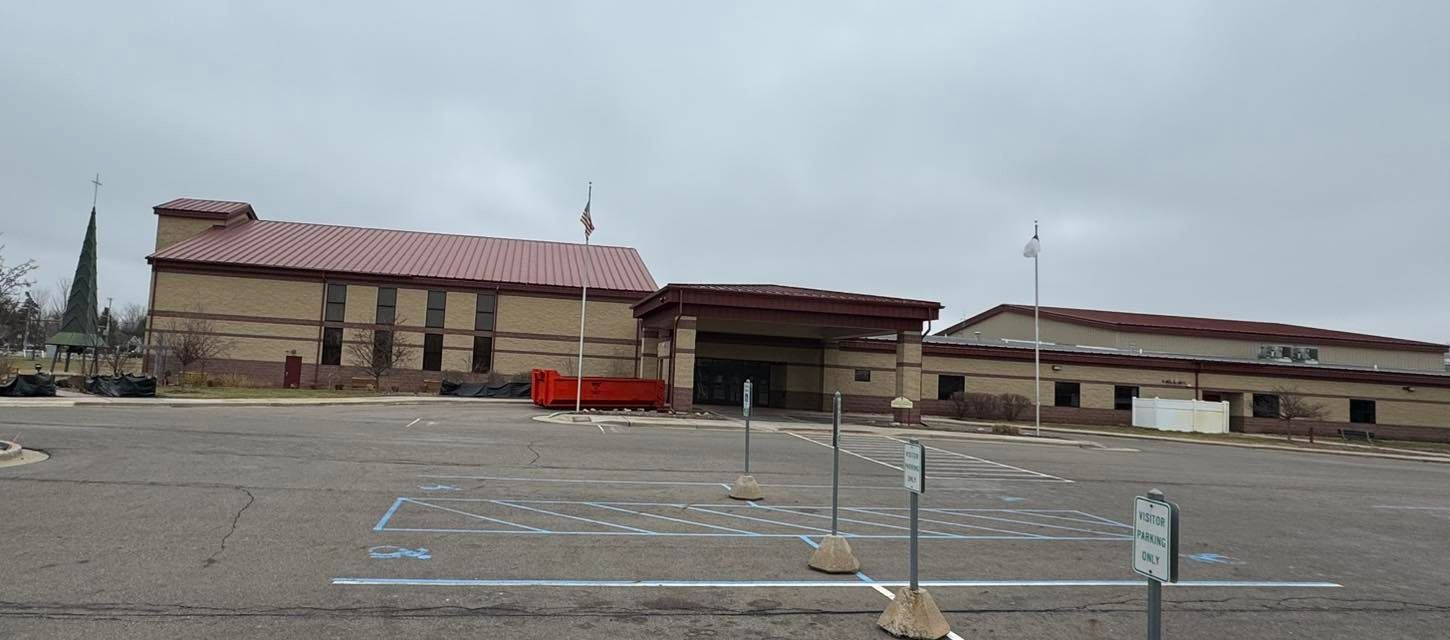 Empty parking lot in front of a low beige building with a red roof and disabled parking spaces.