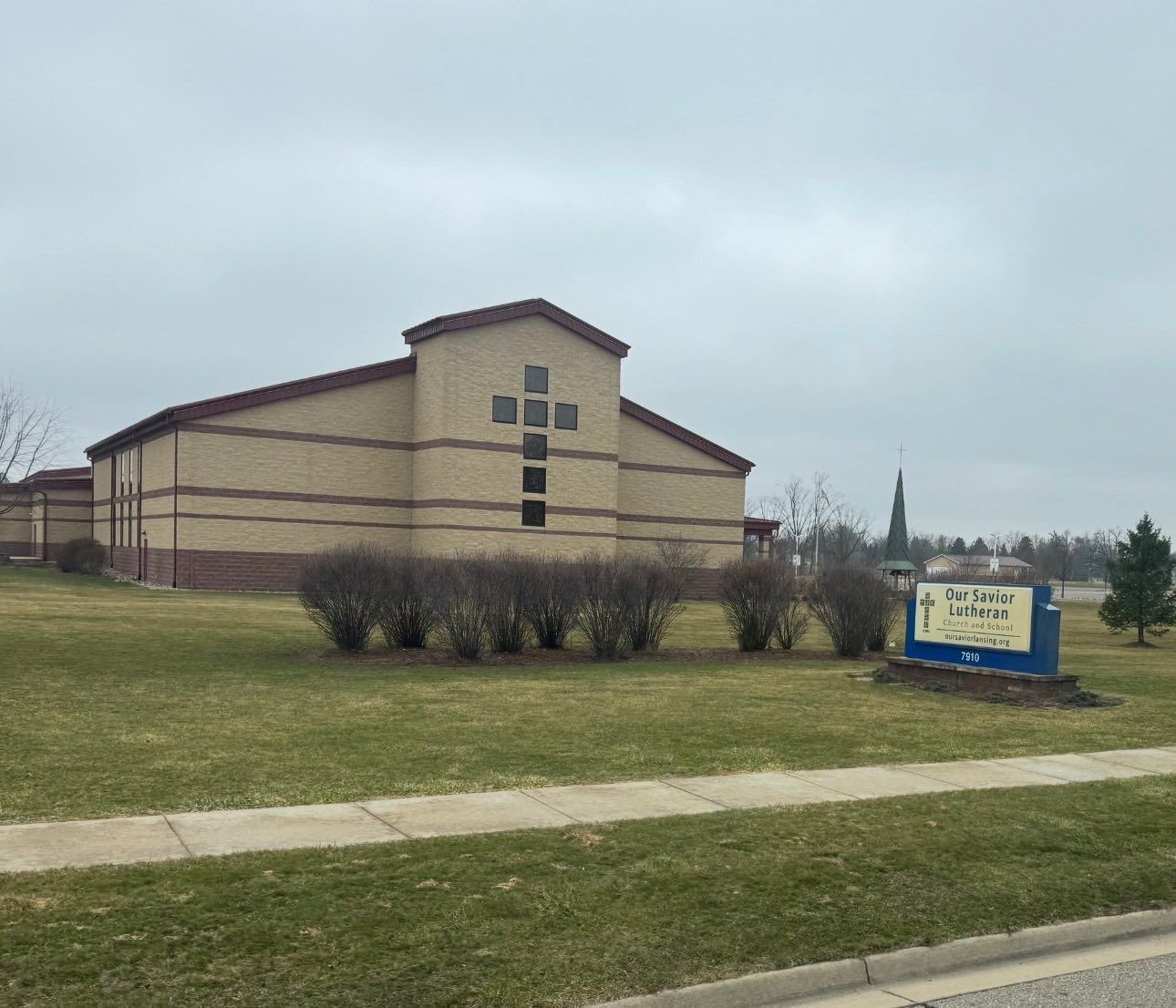 Tan building with a blue sign on a grassy roadside under a cloudy sky