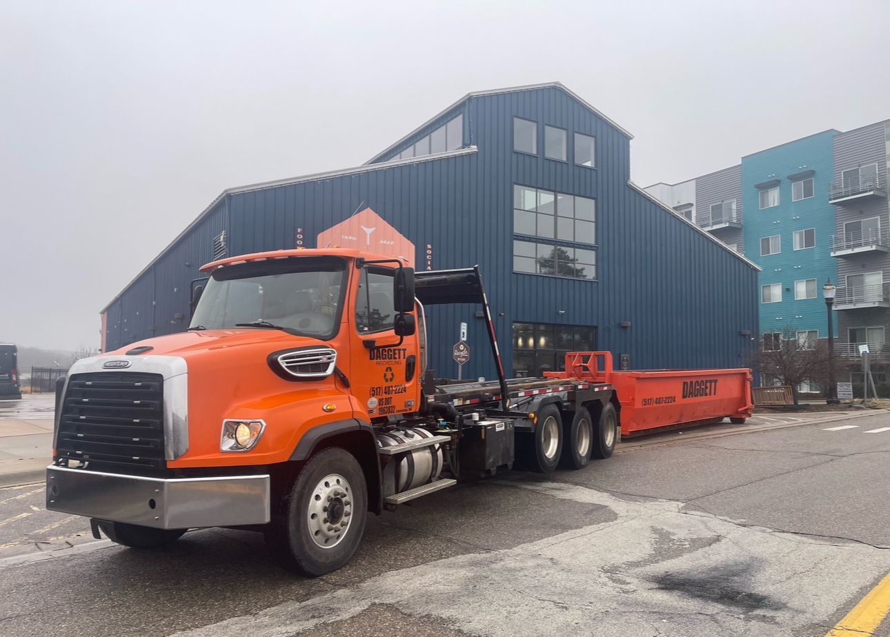 Orange semi truck hauling a long red trailer outside a dark industrial building