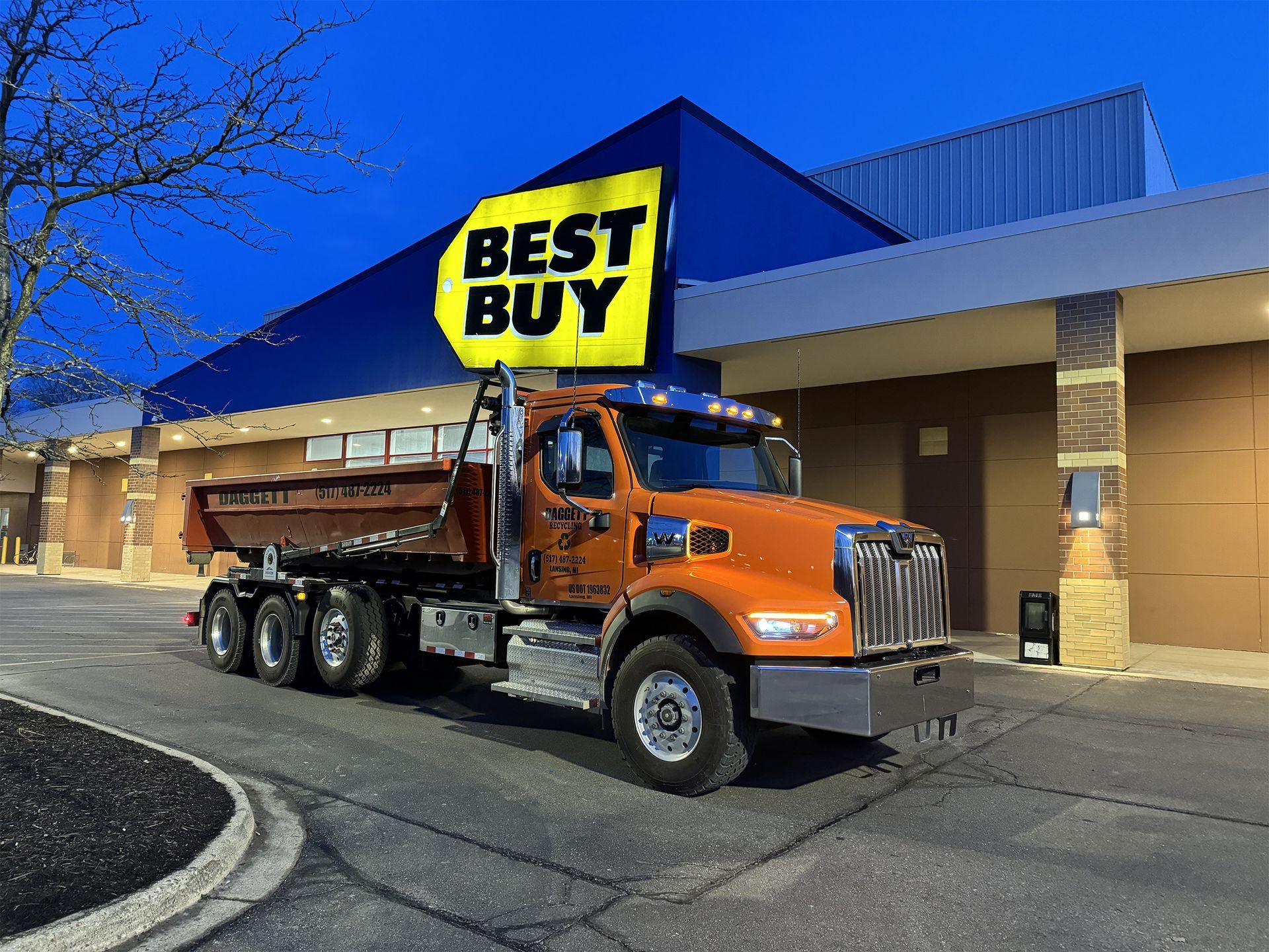 Orange dump truck parked outside a Best Buy store at dusk