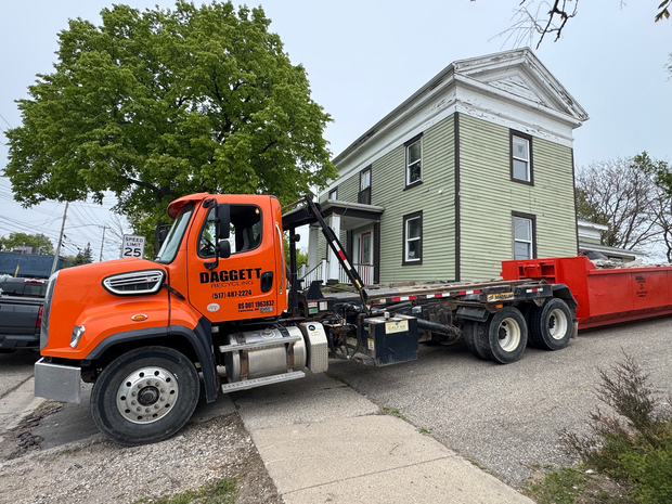 Small brick building with red roof, American flag, and red barricade in front of a covered entrance