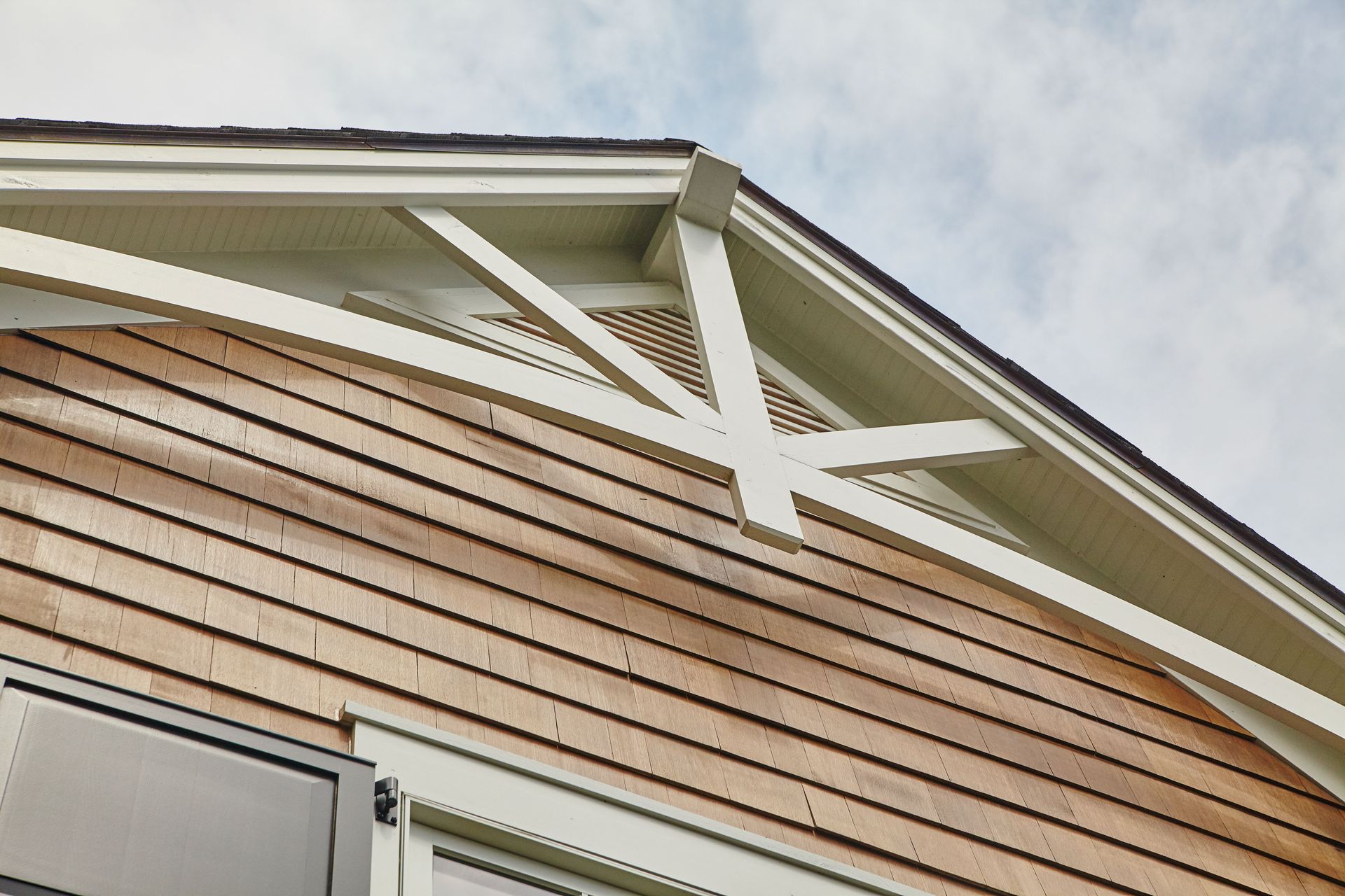 Close-up of a house with light brown wood siding and a decorative white gable with supporting beams.
