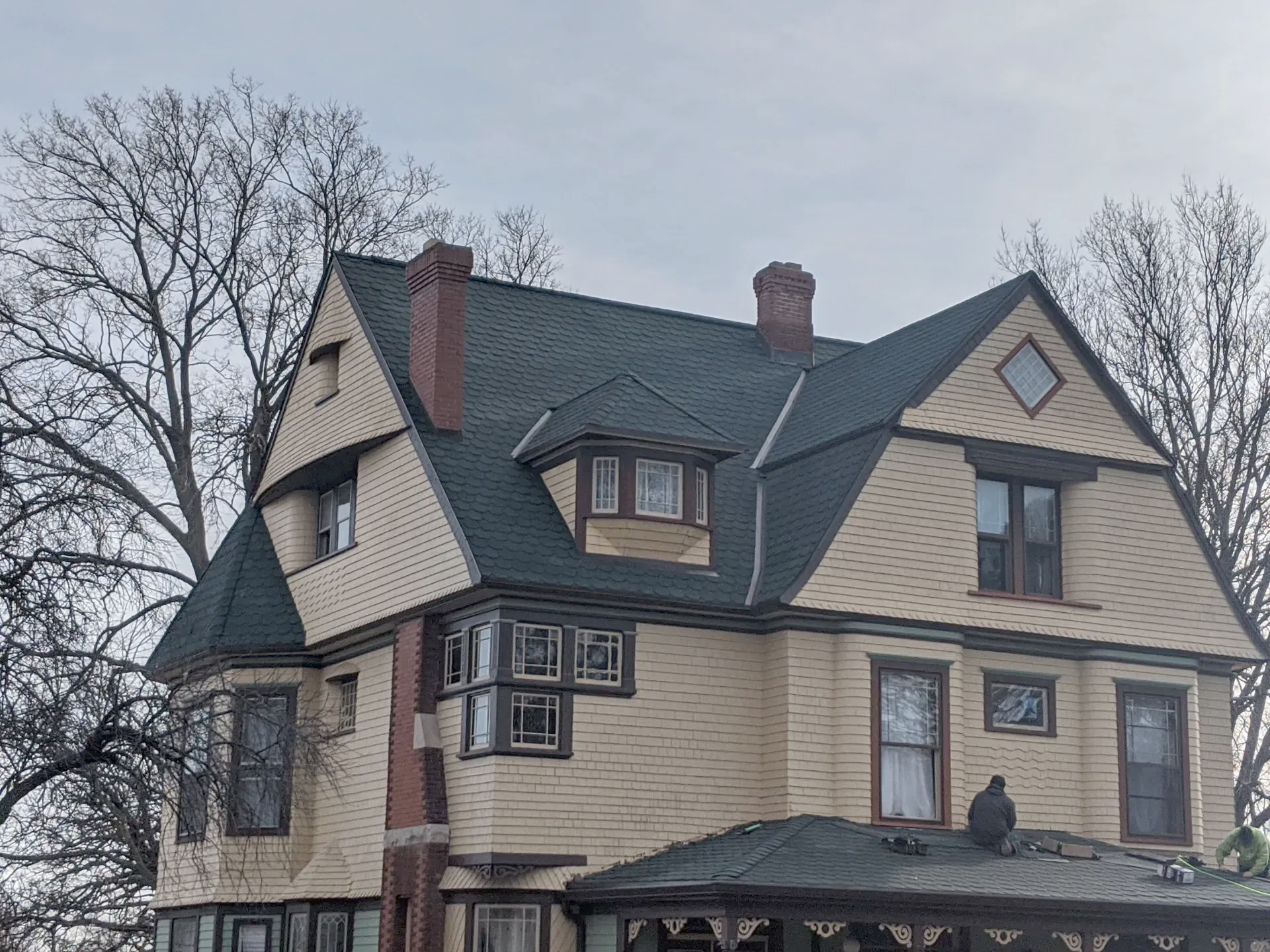 Yellow Victorian house with a dark green roof, chimneys, and bare trees.