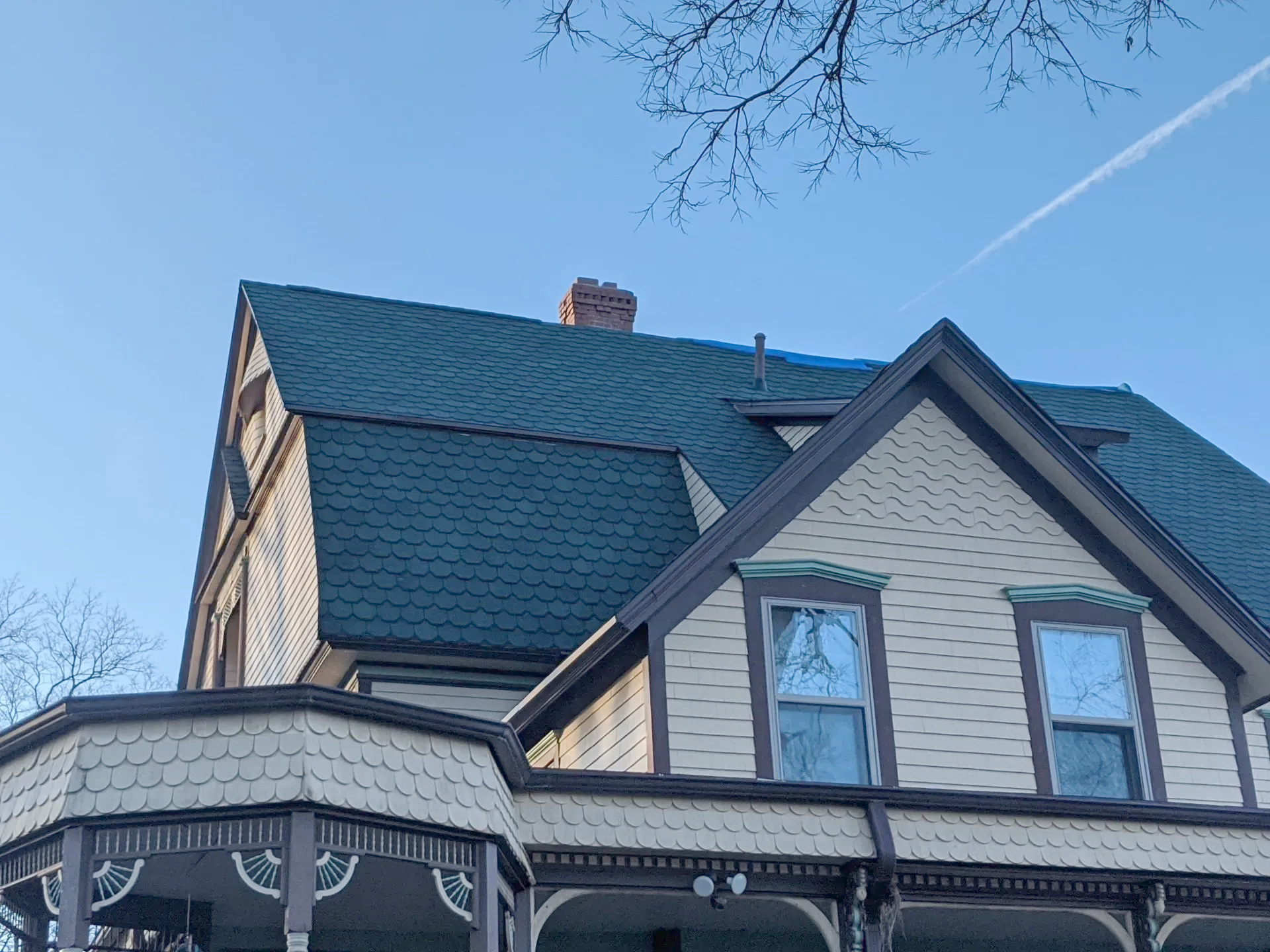 Victorian house with dark green roof and blue tarp against a blue sky, chimney visible.